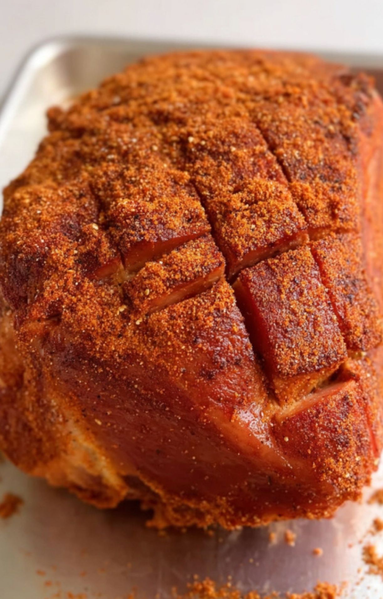 Raw ham scored and coated in a thick layer of homemade pork rub, ready for the smoker.