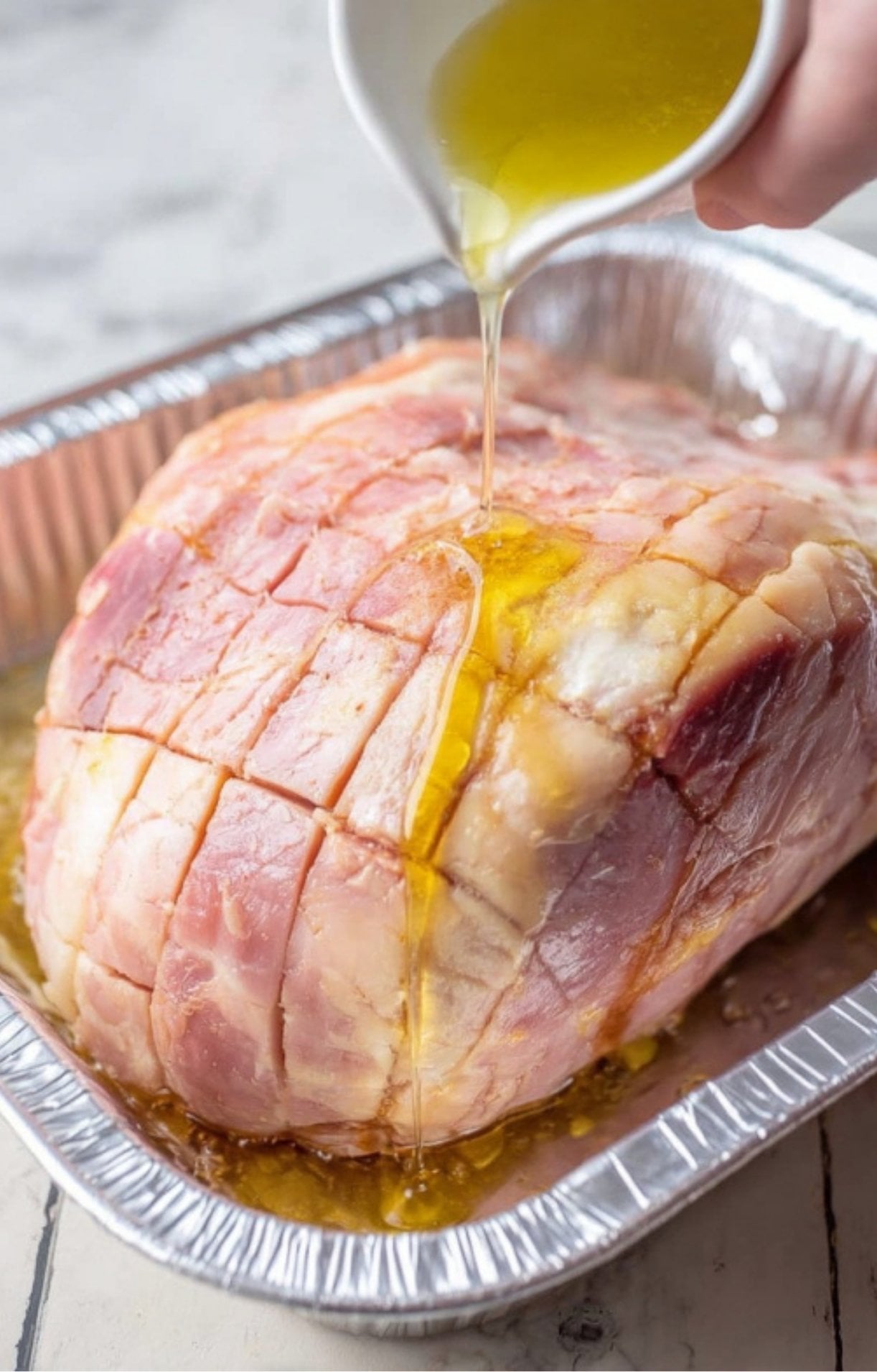 Olive oil being poured over scored ham in a pan, first step in making smoked ham.