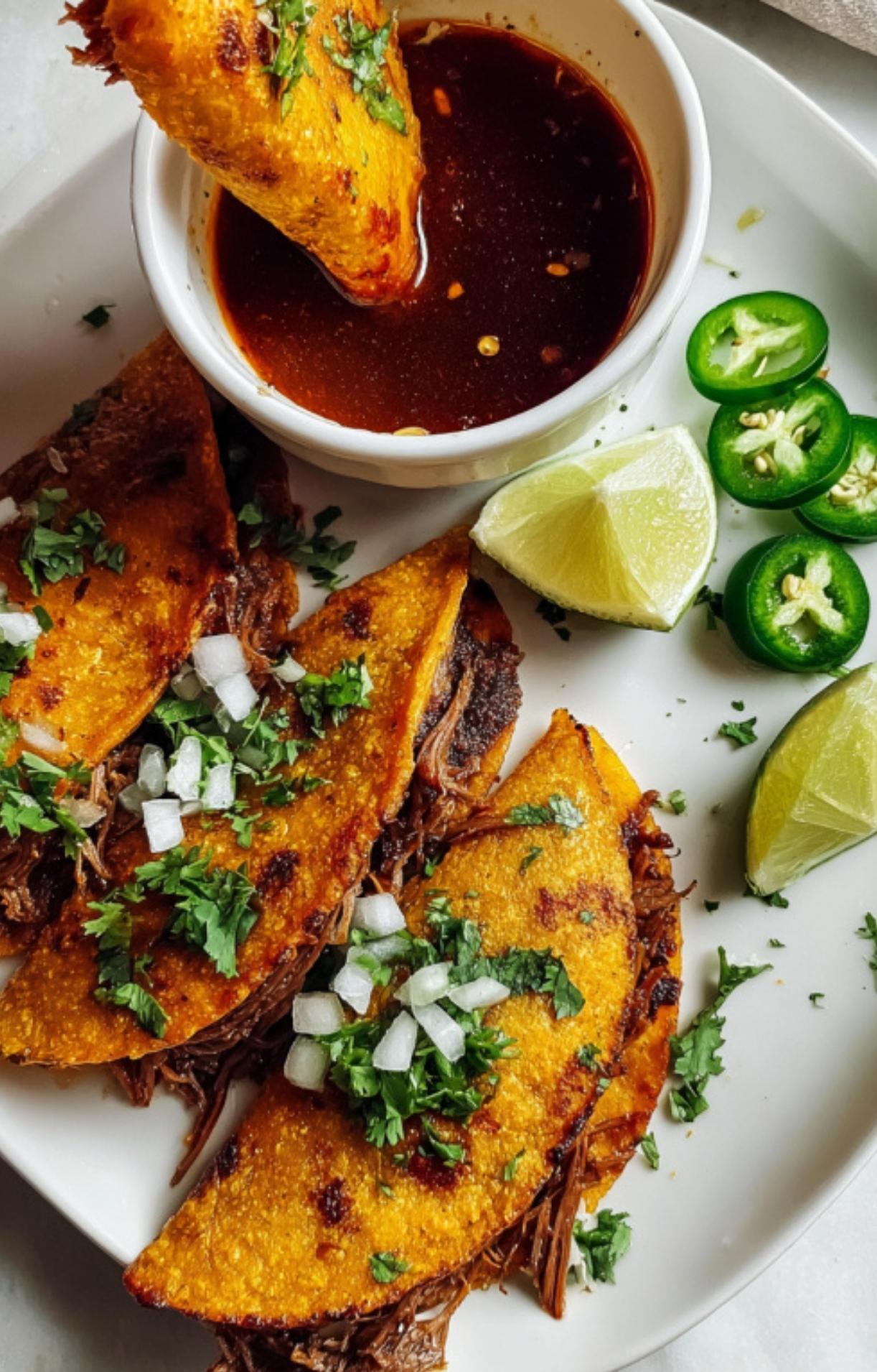 A hand dipping a crispy, golden birria taco into a small bowl of dark red savory consommé.