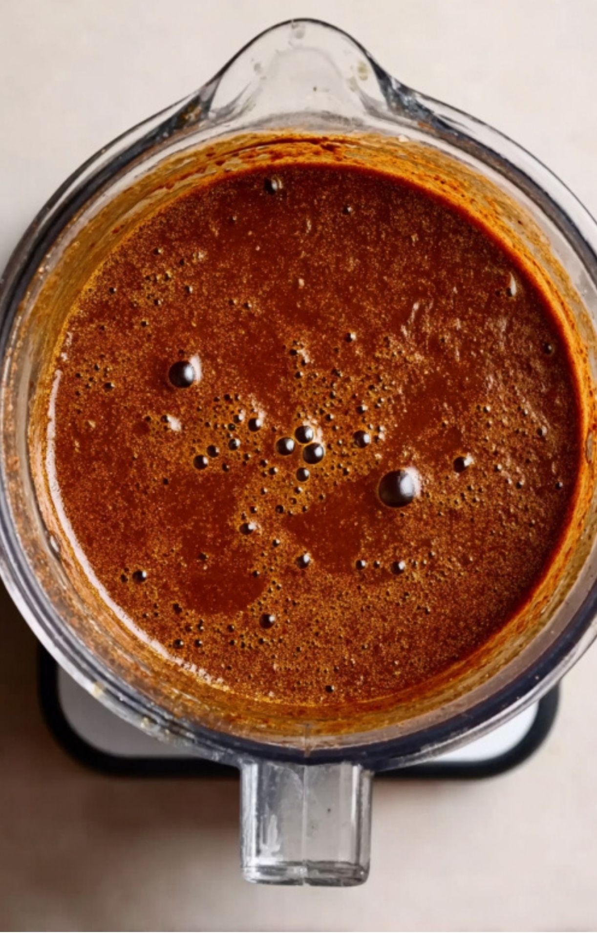 A blender jar filled with a thick, smooth, dark red chili sauce ready to be added to the meat.