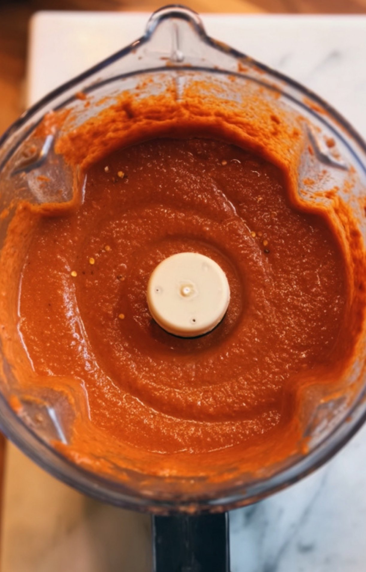 A close-up inside a blender containing a smooth, vibrant deep orange-red chili sauce made from the simmered vegetables and spices.