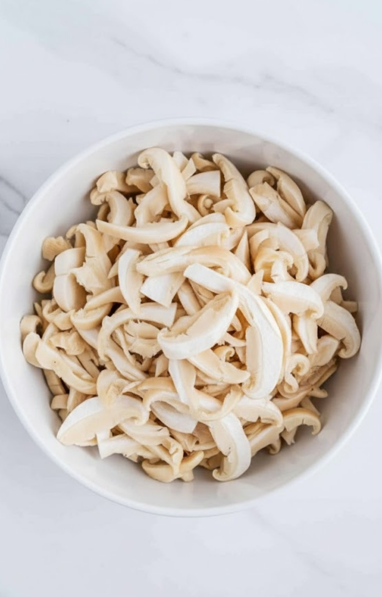 A white bowl filled with raw, hand-shredded king oyster mushrooms mimicking the texture of pulled meat.