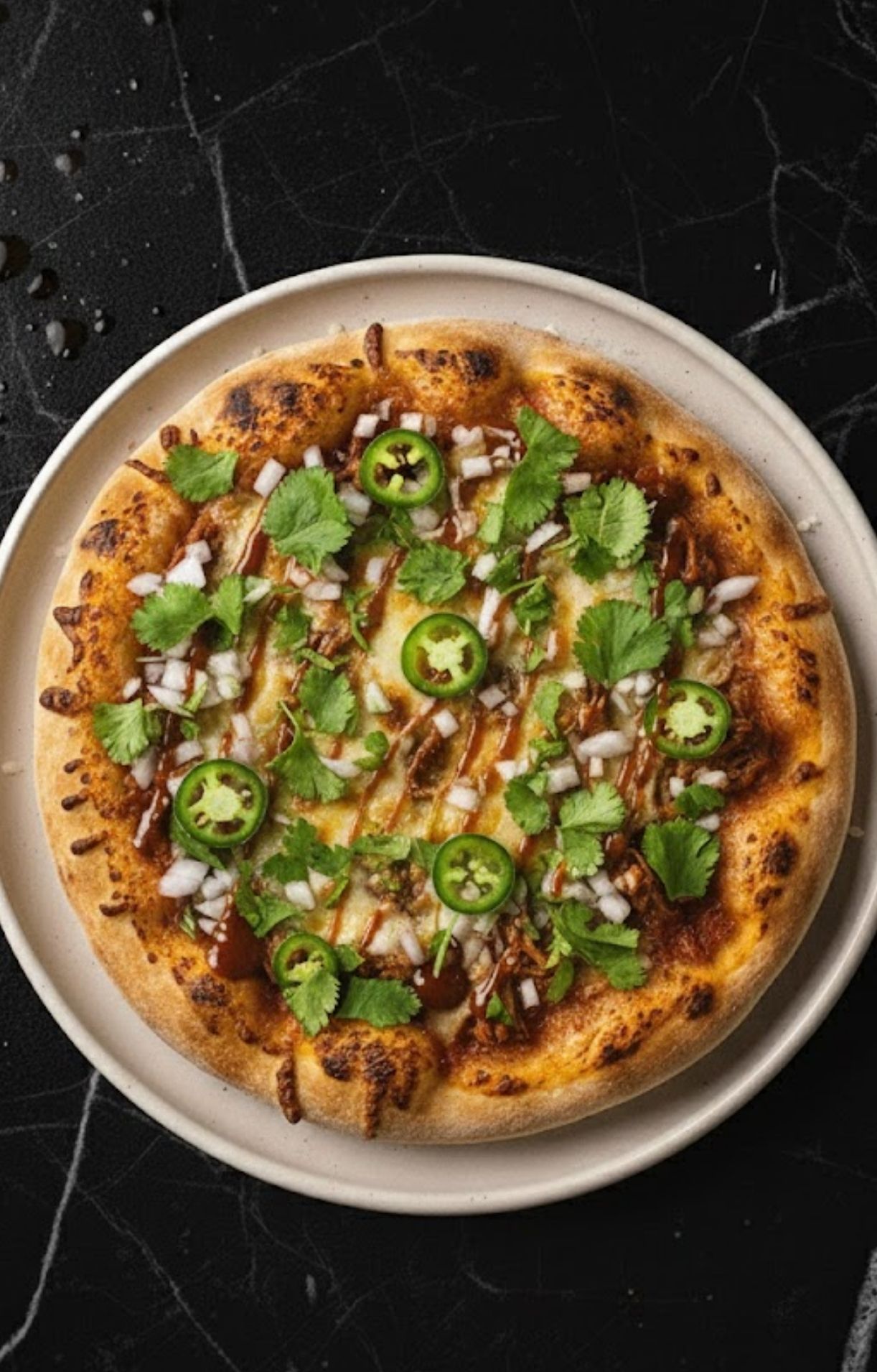 The baked pizza topped with fresh cilantro, diced white onions, and green jalapeño rings.