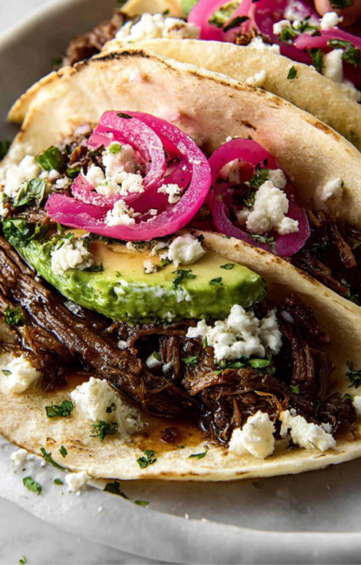 A macro shot focusing on the layers of a taco, showing the shredded beef, a thick slice of avocado, and a sprinkle of fresh cilantro and cheese.