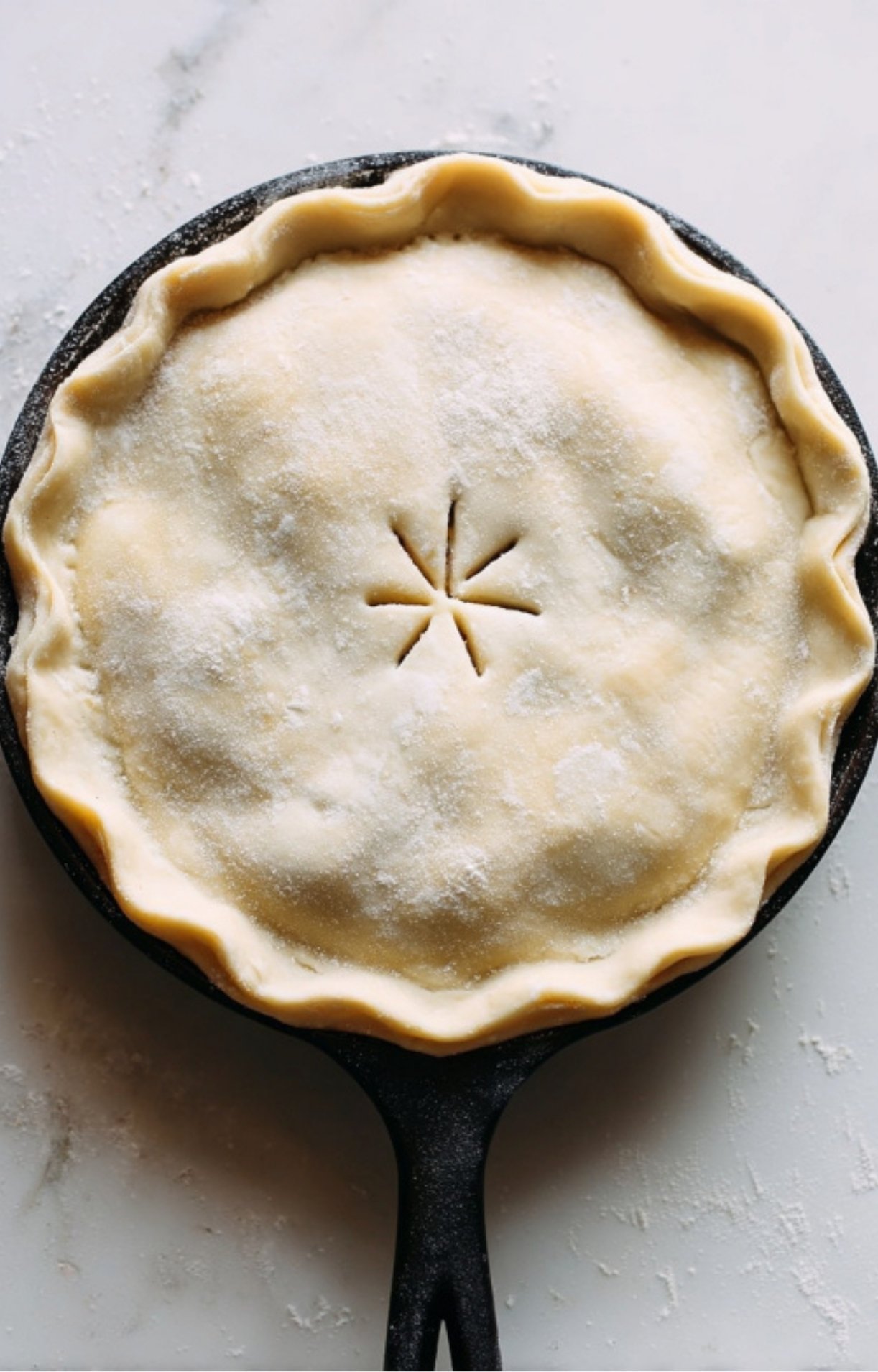 An unbaked pie crust crimped around the edges of a cast-iron skillet with a star-shaped vent cut into the center.