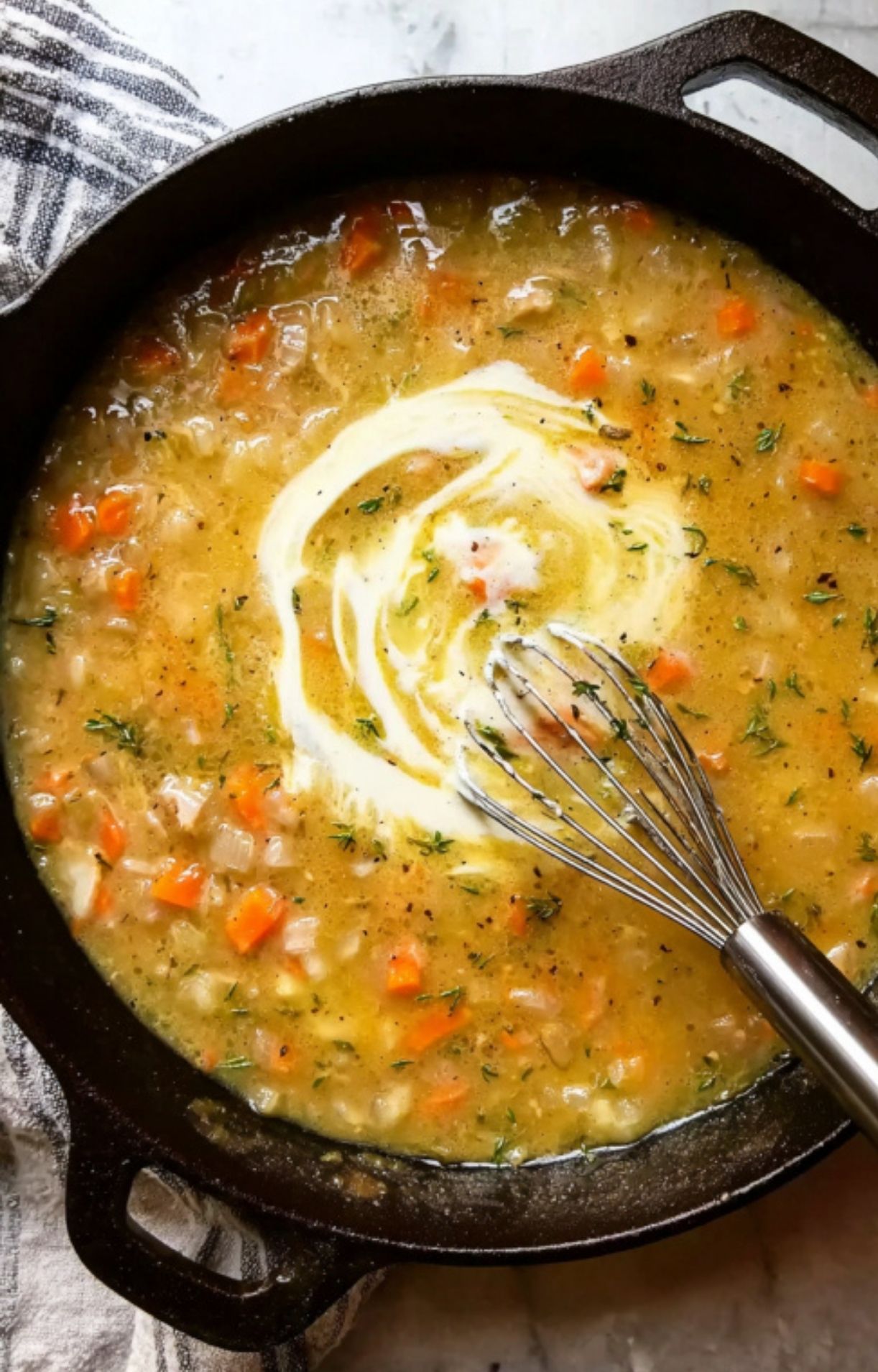 A whisk stirring a creamy white sauce into a simmering vegetable and herb broth in a skillet for Gluten Free Turkey Pot Pie.