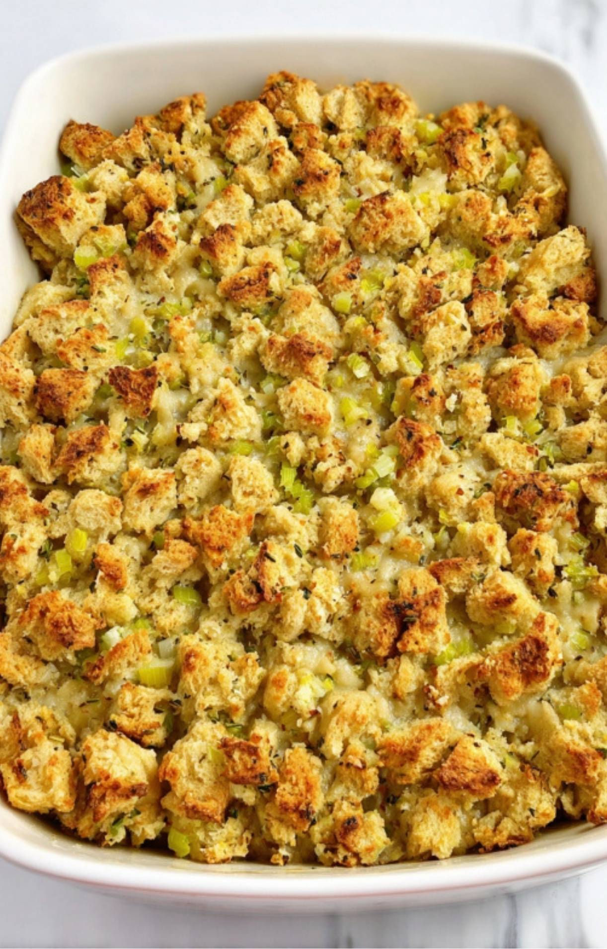 A white baking dish filled with turkey pot pie filling and completely covered with a layer of herb-seasoned bread stuffing and celery pieces before baking