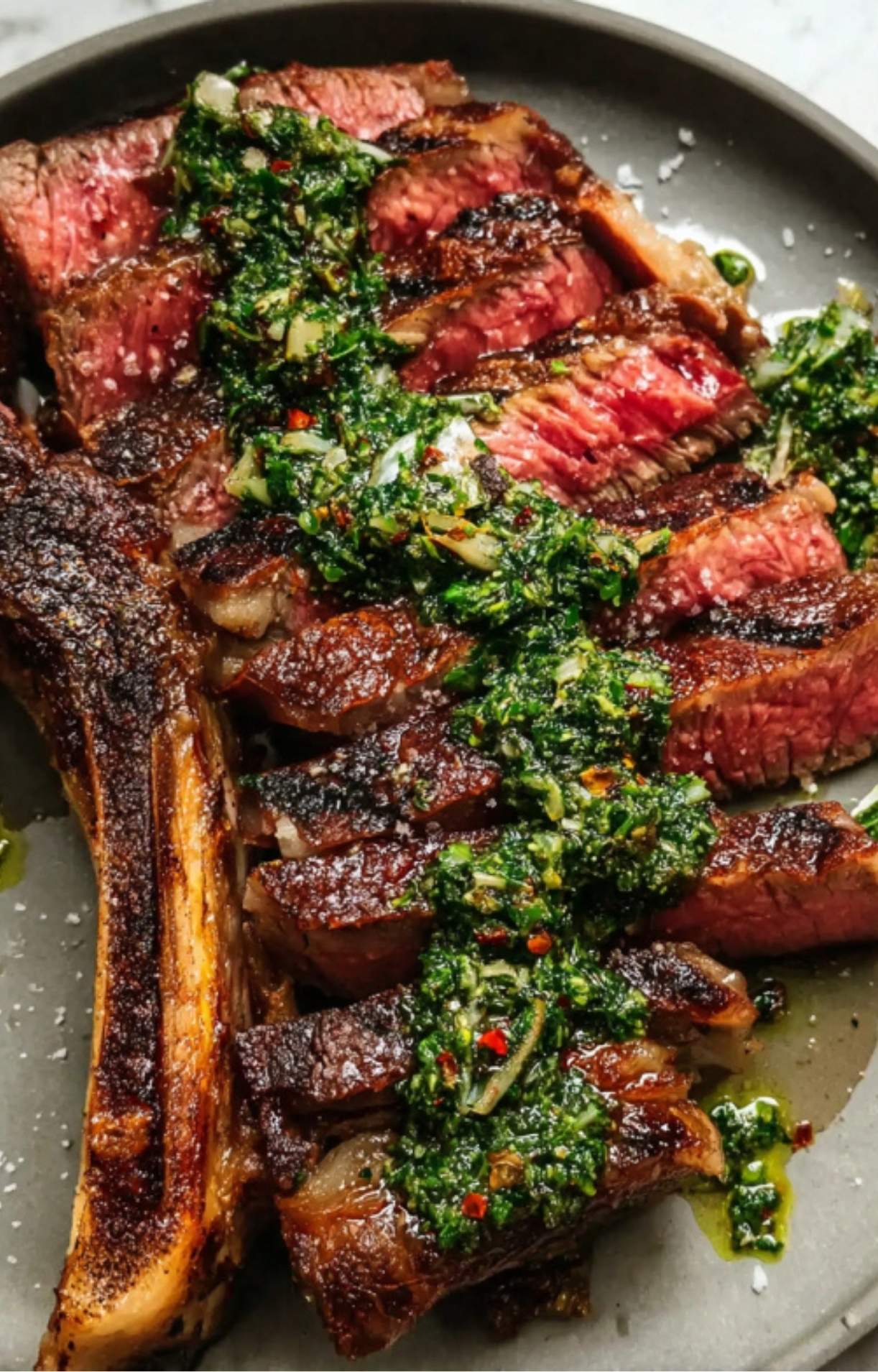 Slices of juicy medium-rare rib eye steak arranged on a plate and topped with a vibrant, zesty green herb salsa.