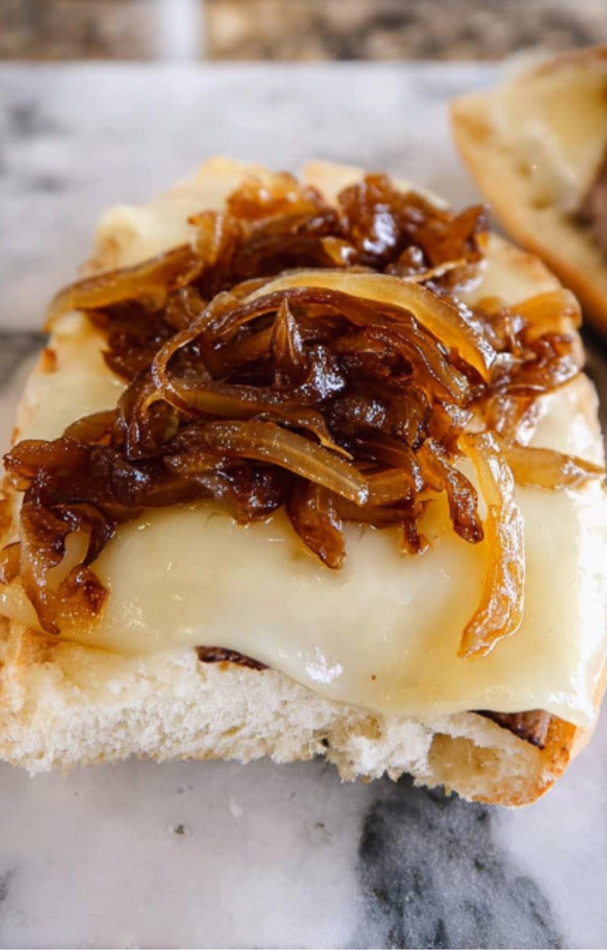 A close-up of a slice of bread with melted cheese topped with a generous portion of caramelized onions.