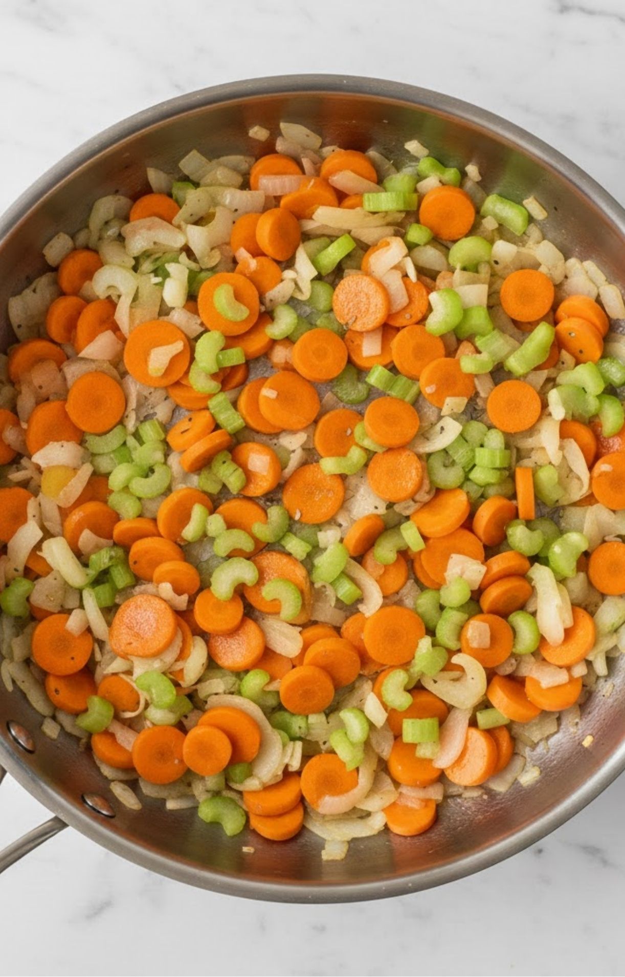 A stainless steel skillet filled with sliced carrots, celery, and onions being sautéed in oil for a keto turkey pot pie base.