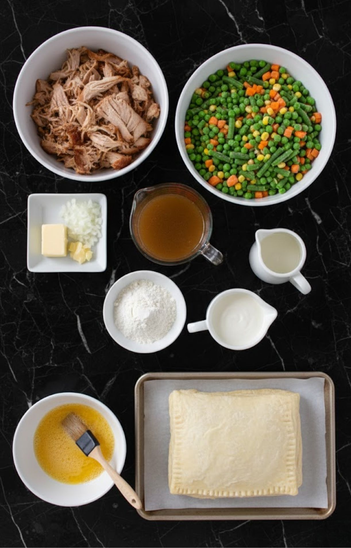An overhead view of ingredients for Smoked Turkey Pot Pie including shredded turkey, frozen vegetables, broth, cream, flour, and puff pastry.