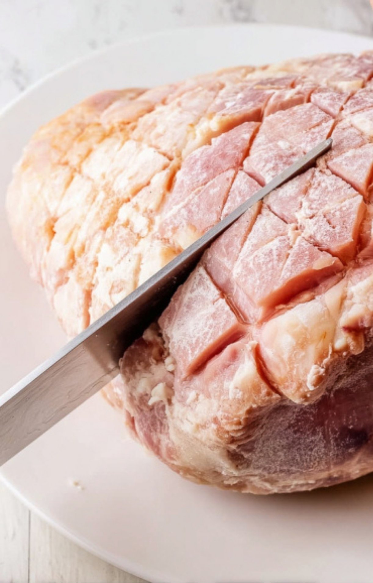 Knife scoring a ham in a diamond pattern to help glaze soak in during smoking.