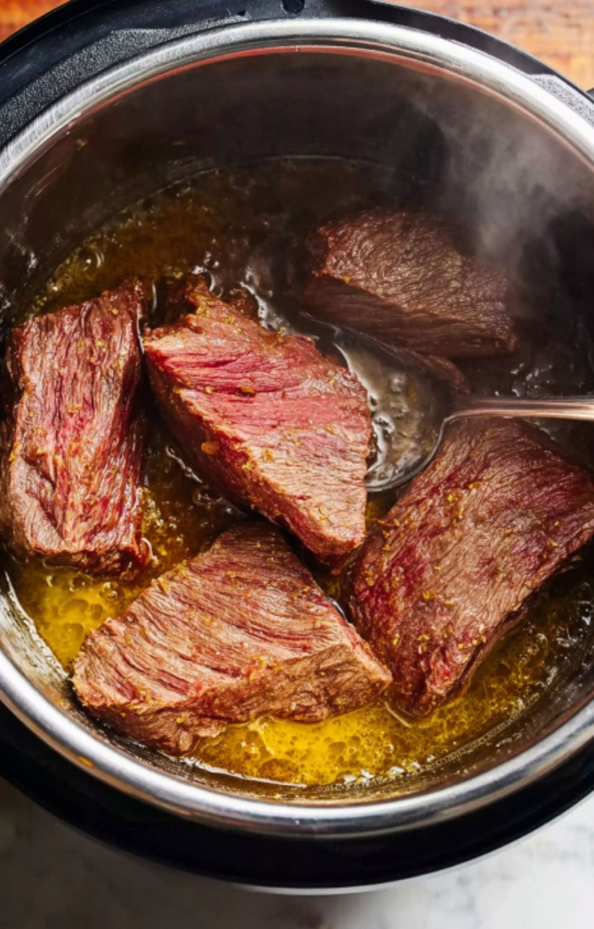 Large seasoned chunks of beef being seared in a small amount of oil inside the Instant Pot until browned on the edges.