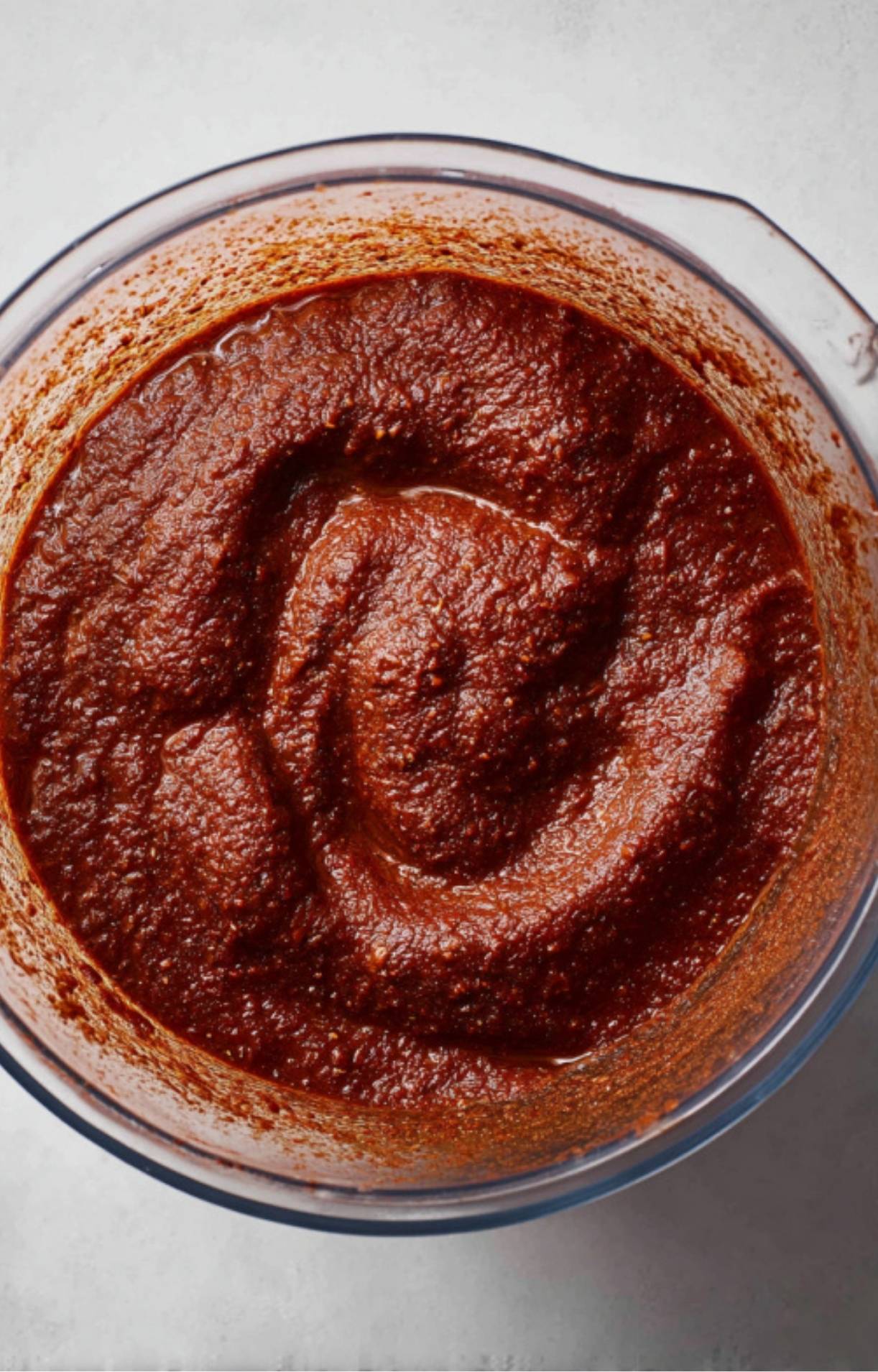 A close-up of a blender filled with a smooth, deep red birria sauce made from blended peppers and spices.