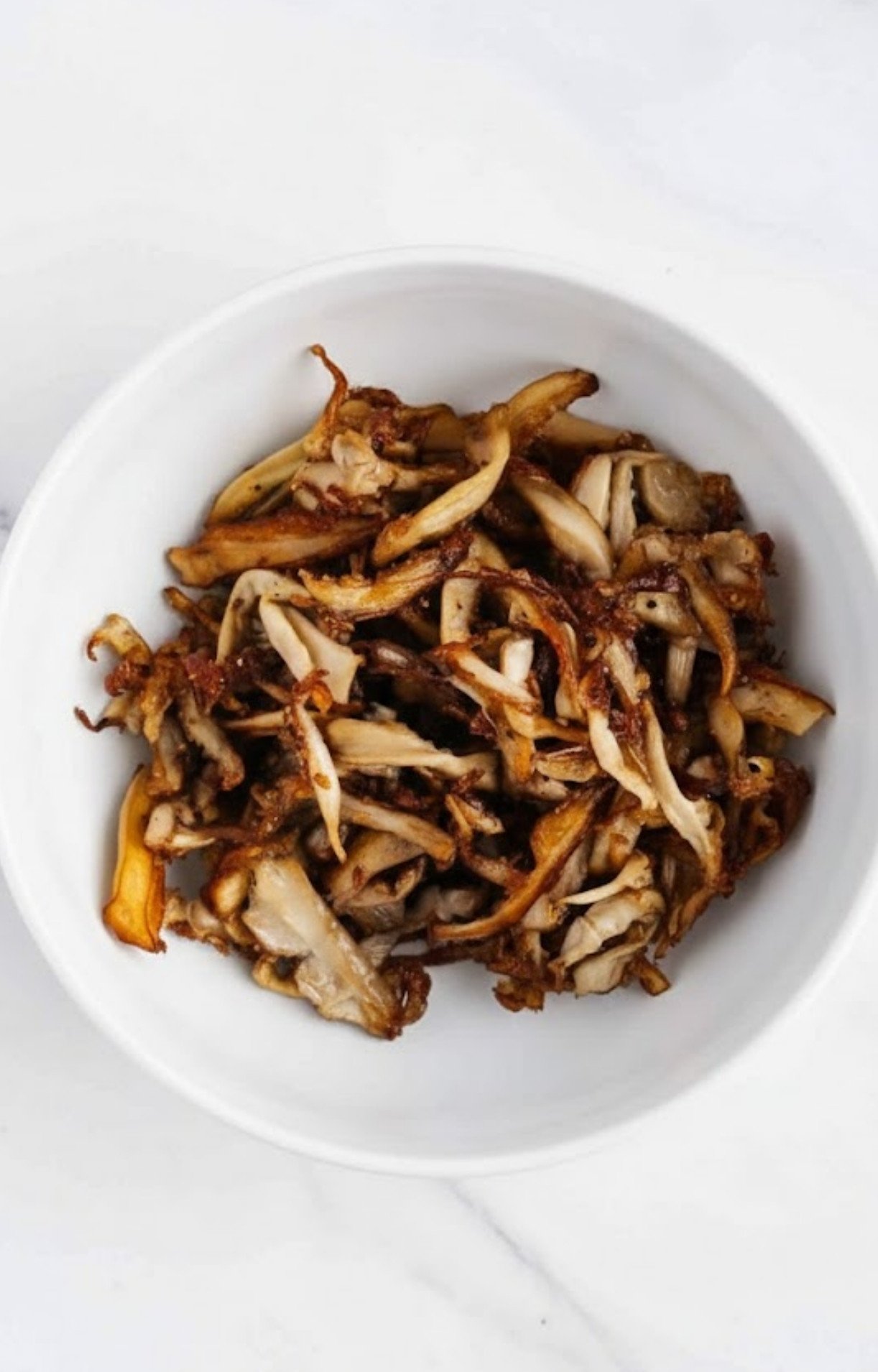 Sautéed and browned shredded mushrooms in a bowl, showing caramelized edges and a meaty texture.