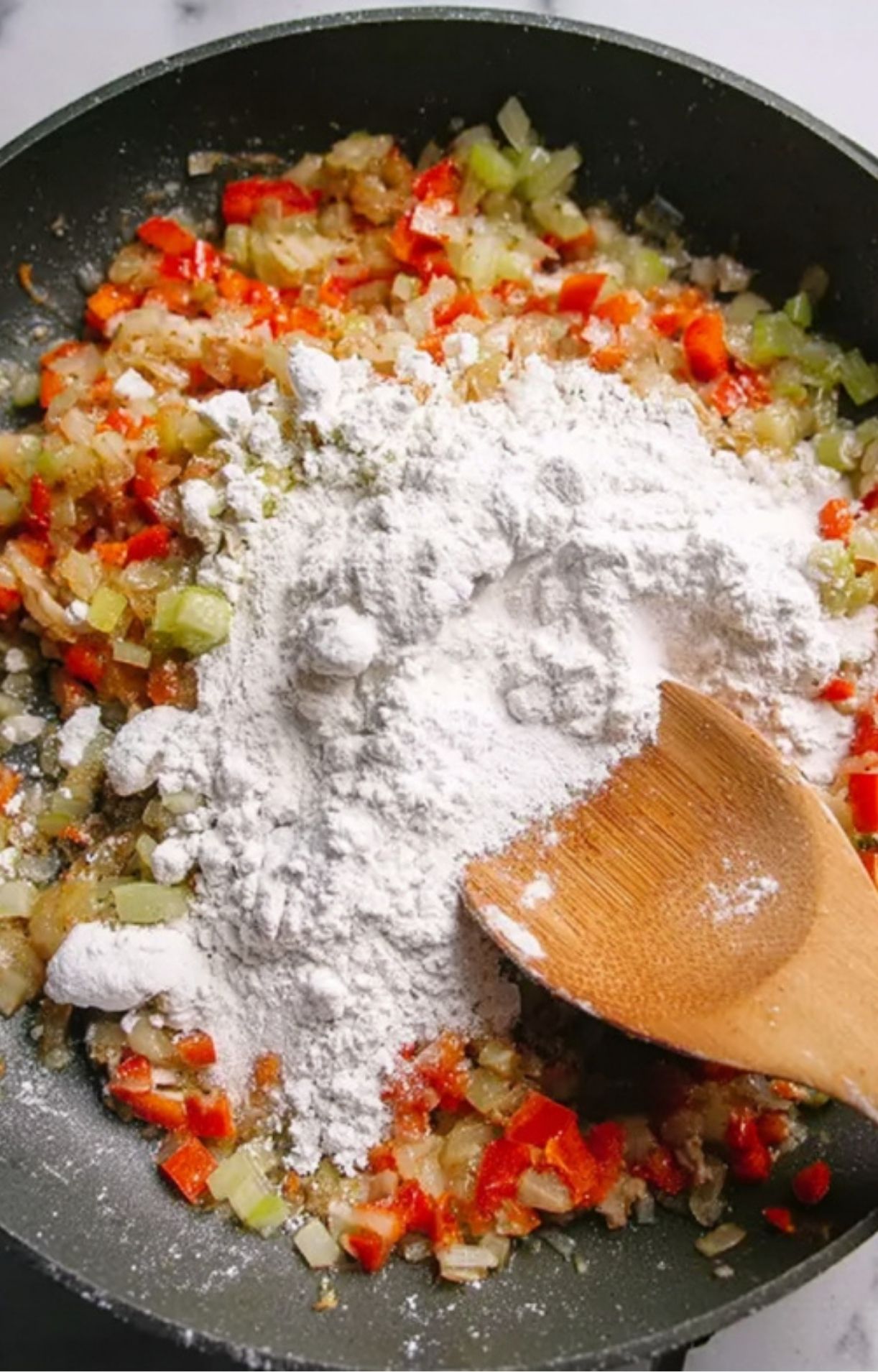 A generous amount of white flour being added to the sautéed vegetables in the pan to thicken the Turkey Pot Pie with Crescent Rolls.