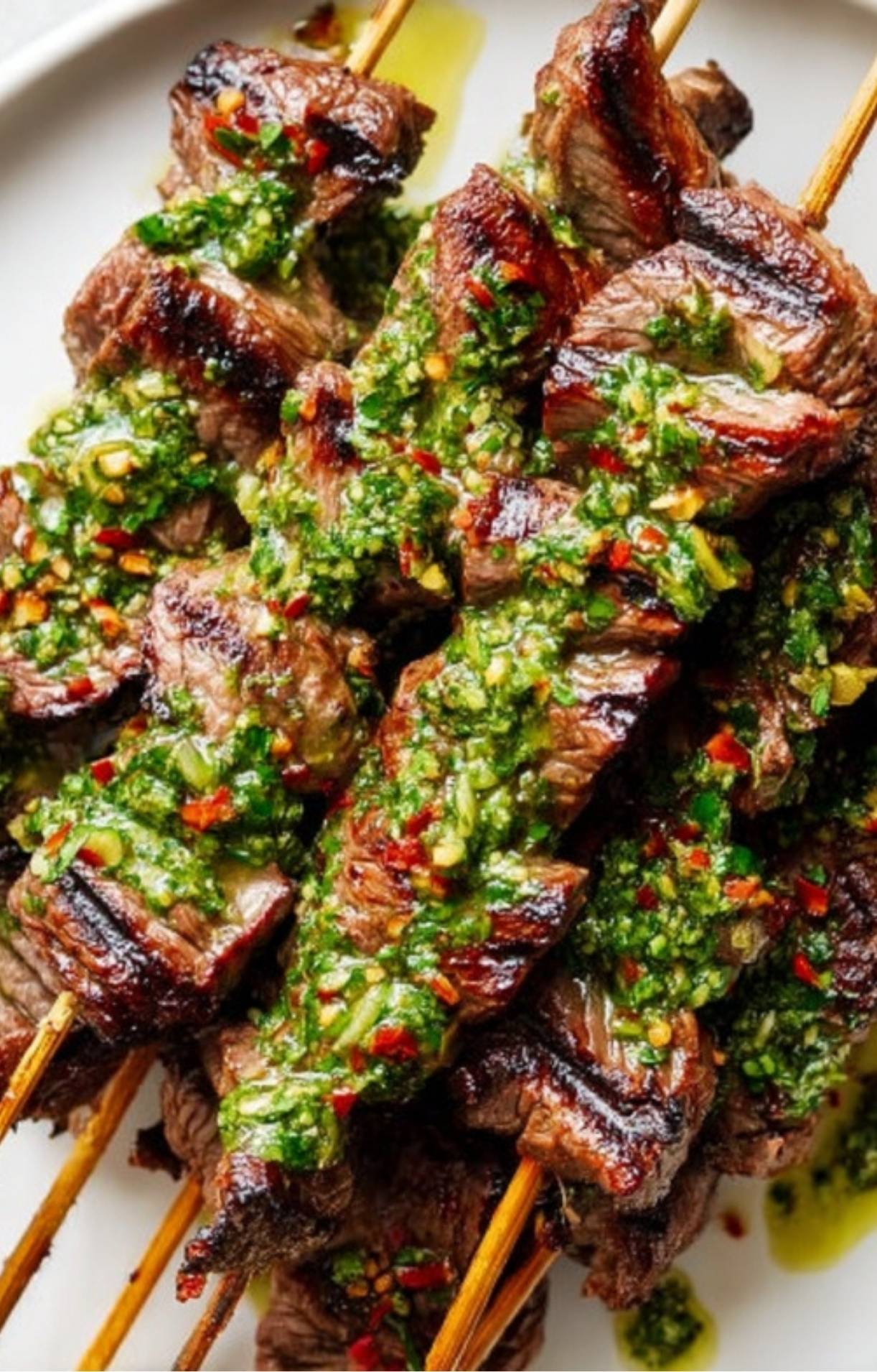 Close-up shot of tender steak skewers generously drizzled with chimichurri sauce.
