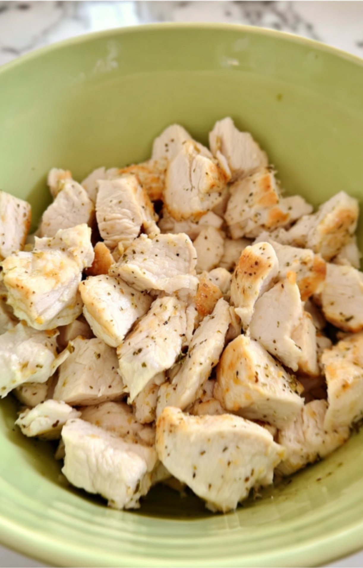 A green bowl filled with perfectly seasoned, cooked turkey breast cubes ready to be mixed into a keto pot pie filling.