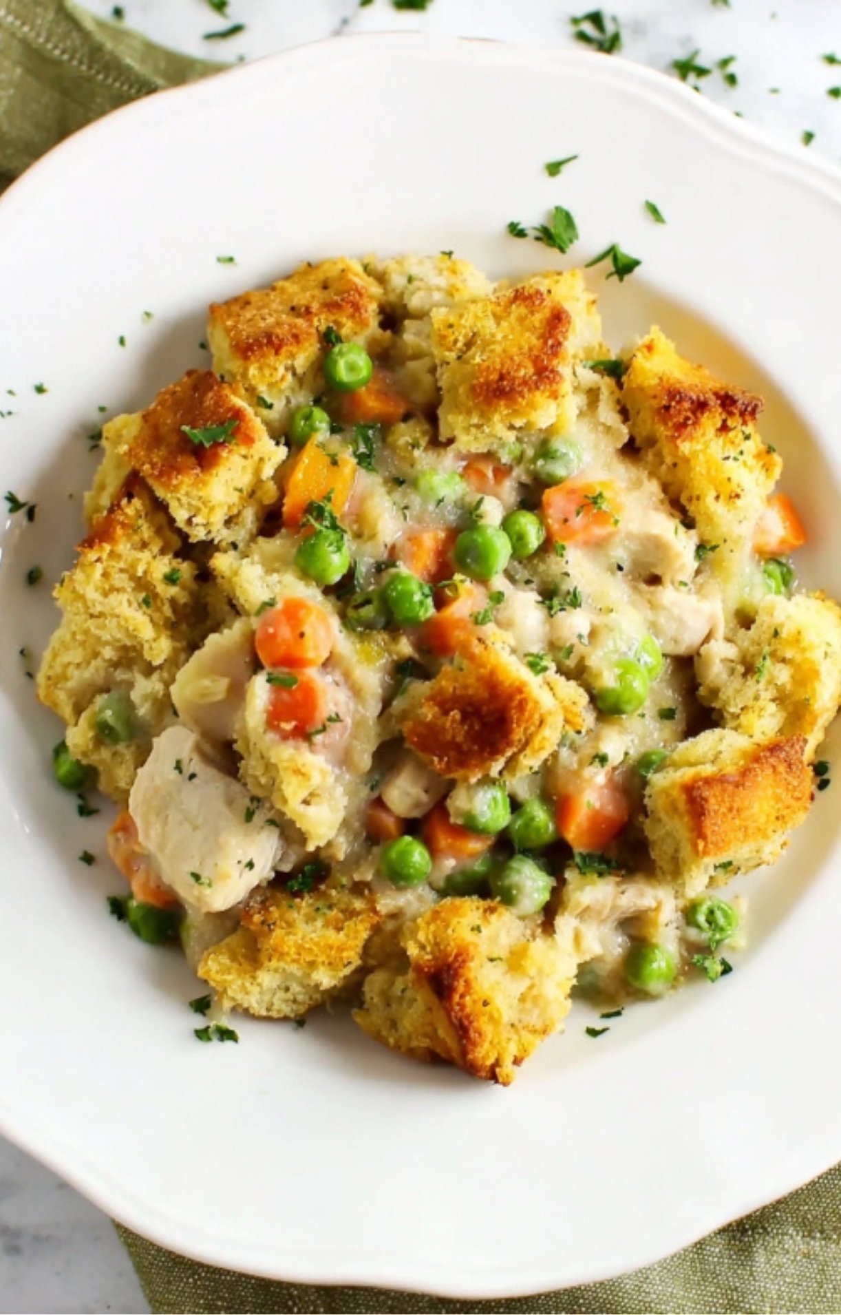 A single serving of turkey pot pie with a crispy stuffing crust on a white plate, garnished with fresh parsley.