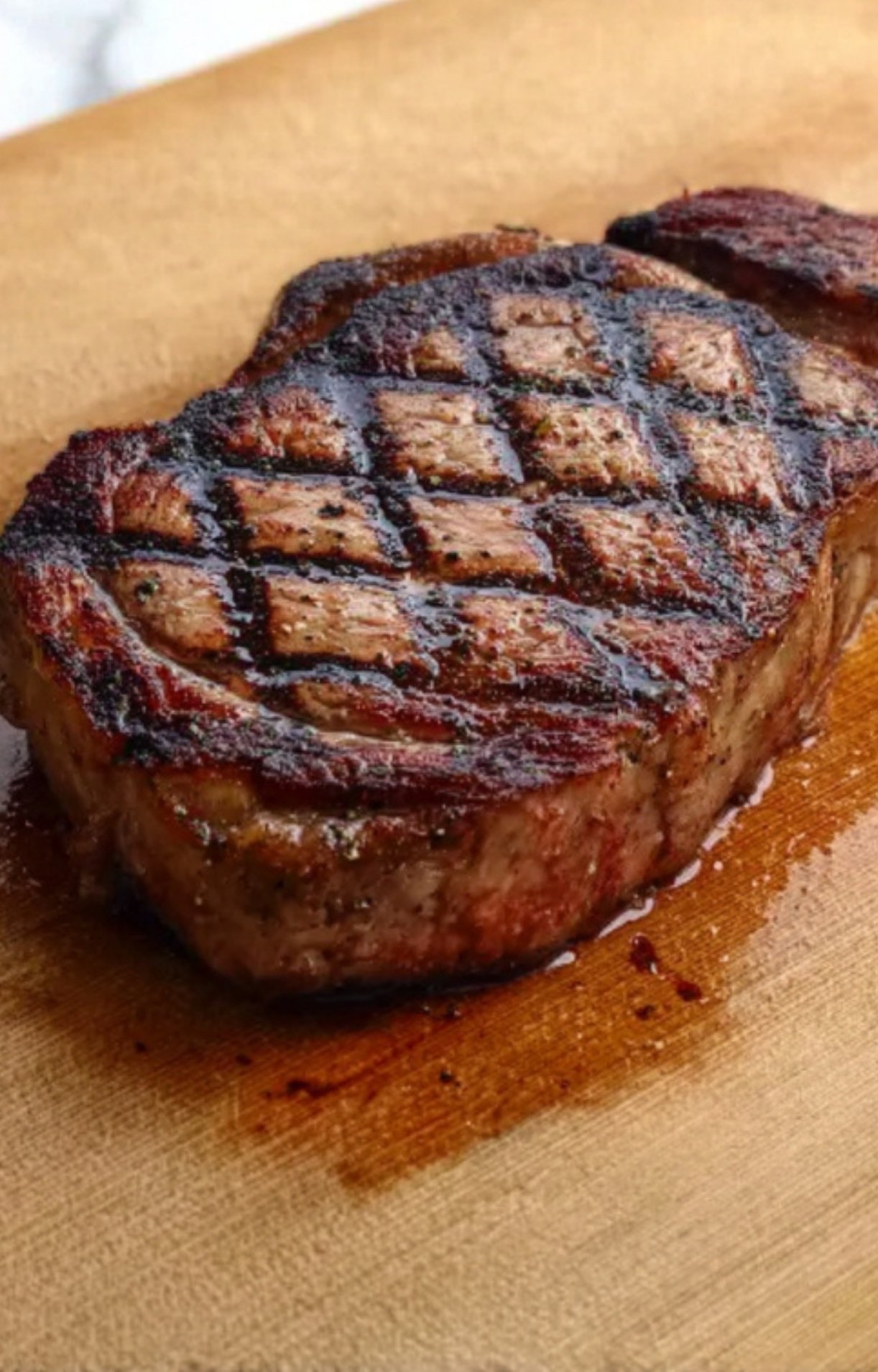 Ribeye steak with diamond grill marks resting on a wooden board. Ideal for pairing with homemade chimichurri sauces.