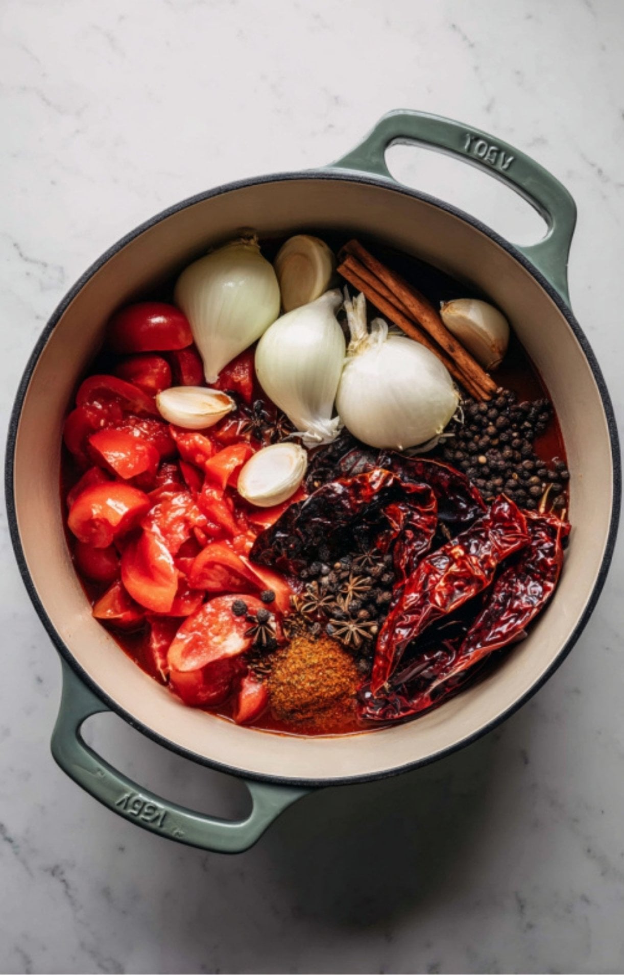 A pot filled with chopped tomatoes, onions, garlic, cinnamon sticks, dried chilies, and whole peppercorns.