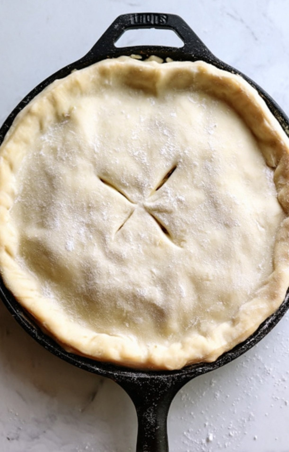 Raw puff pastry dough covering the skillet, tucked at the edges with a cross-shaped vent cut in the center.