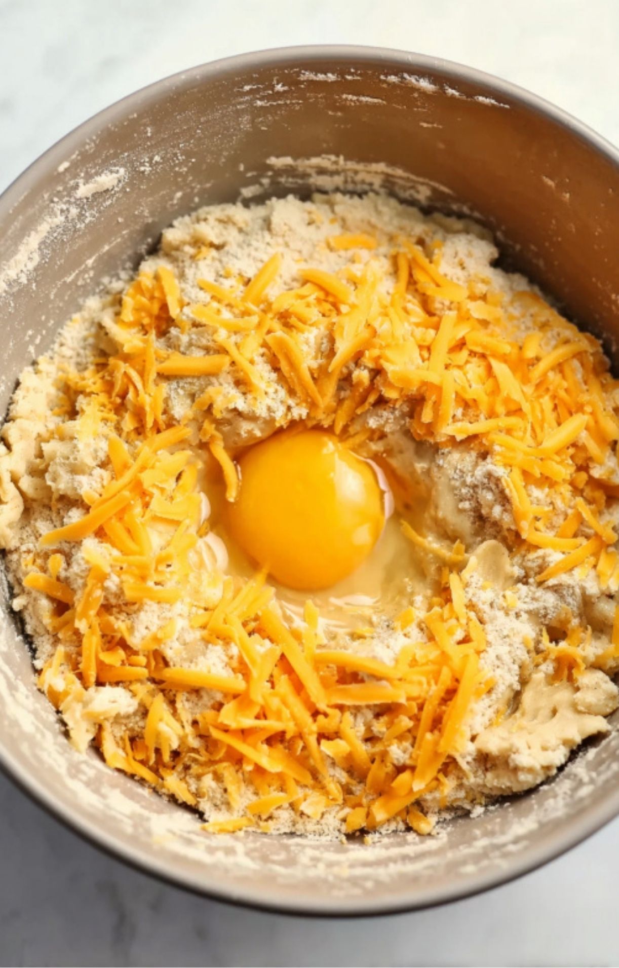 A bowl of almond flour, shredded cheddar cheese, and a fresh egg yolk being mixed together to form the crust for a keto turkey pot pie.