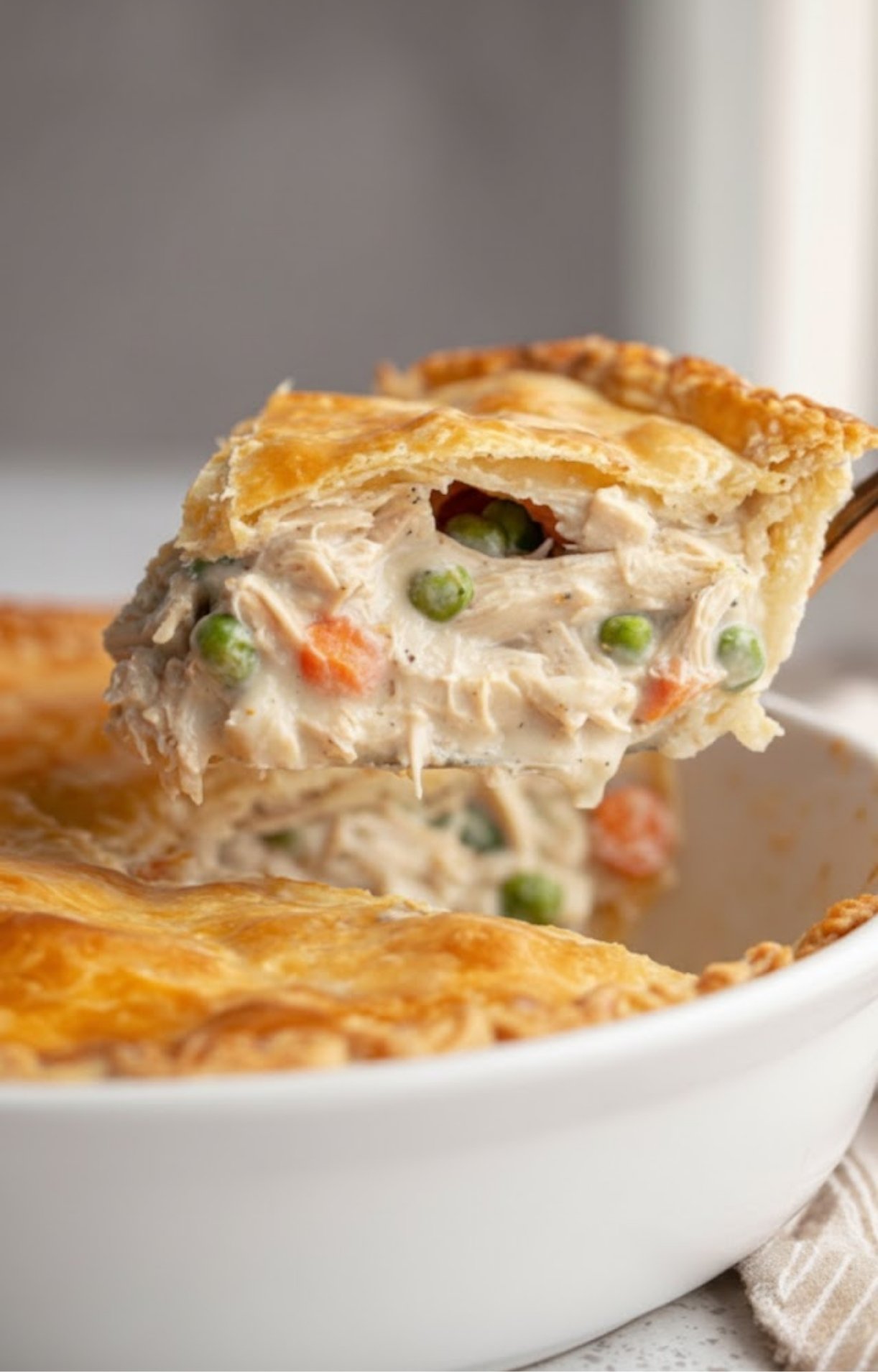 A golden, flaky slice of Dad’s Turkey Pot Pie being lifted out of a glass baking dish, revealing a creamy interior filled with shredded turkey, peas, and carrots.