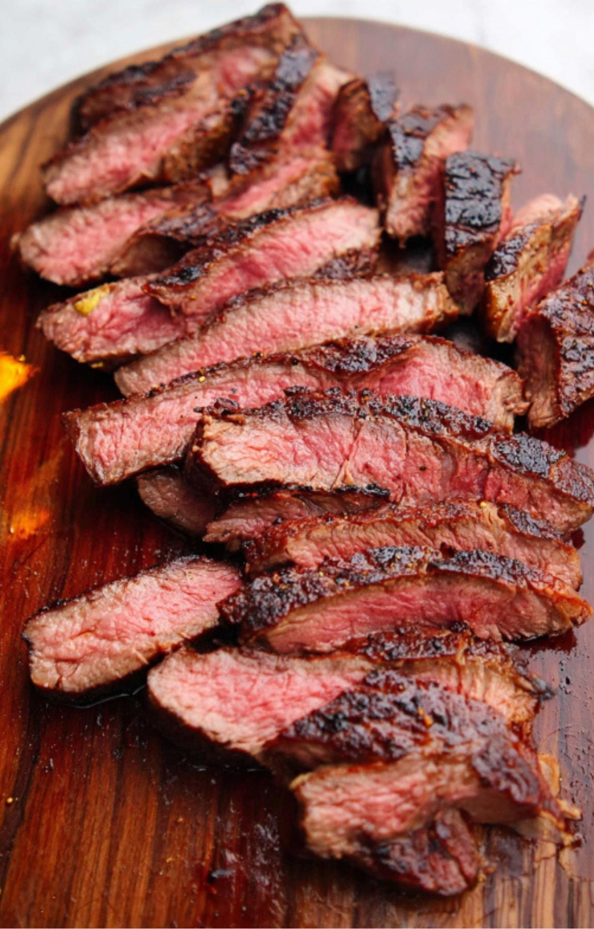 Juicy grilled steak sliced into strips on a wooden cutting board, showing a pink, tender center and a crispy, charred crust.