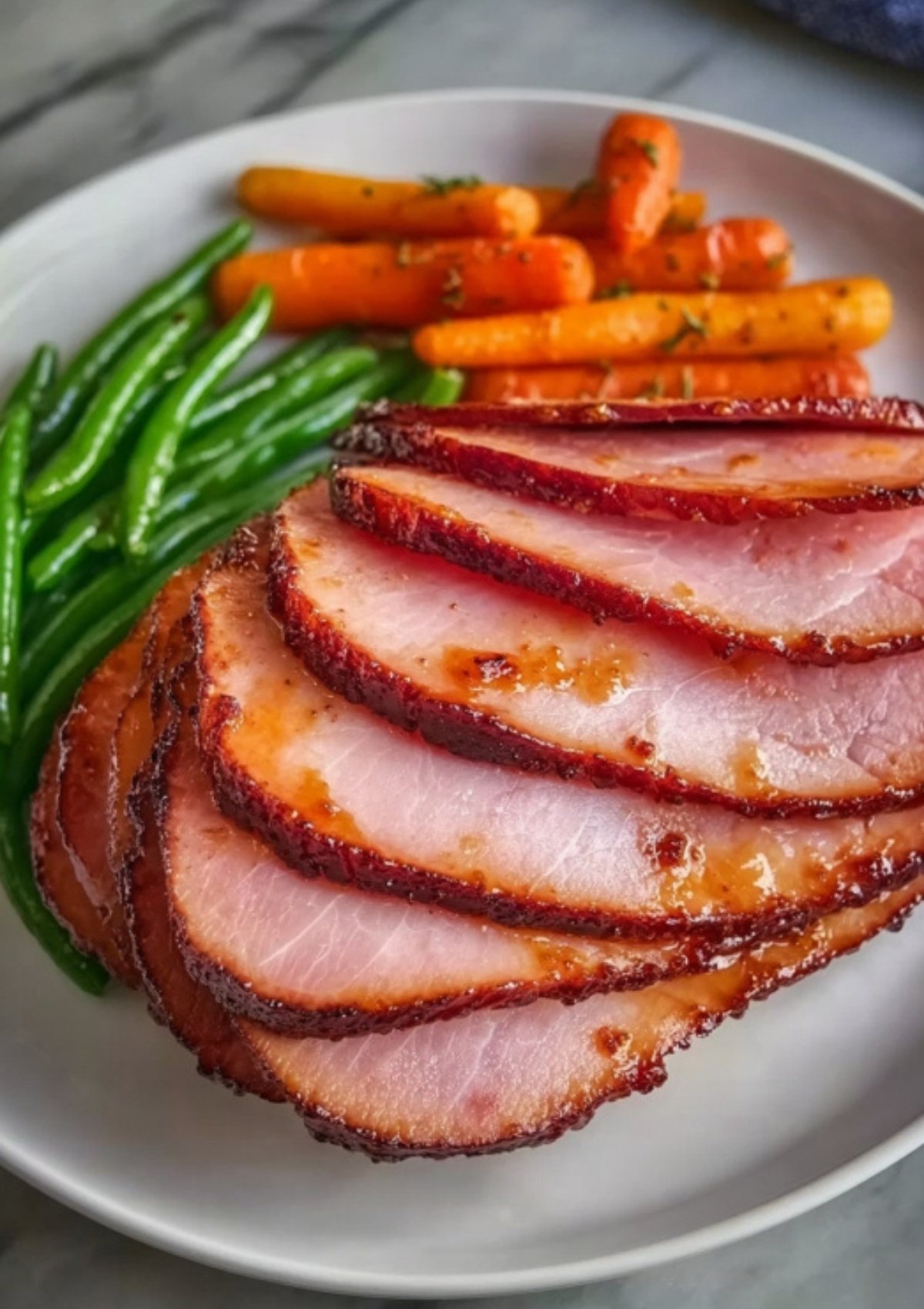 Sliced smoked ham served with green beans and carrots, classic holiday meal