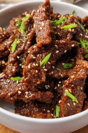 A white bowl filled with crispy Air Fryer Beijing Beef strips garnished with sesame seeds and fresh green onions.