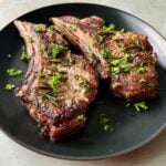 Two seared air fryer lamb shoulder chops served on a black plate with fresh herb garnishes.