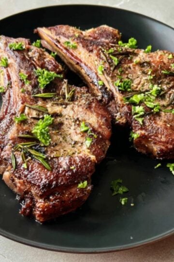 Two seared air fryer lamb shoulder chops served on a black plate with fresh herb garnishes.