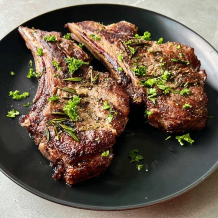 Two seared air fryer lamb shoulder chops served on a black plate with fresh herb garnishes.