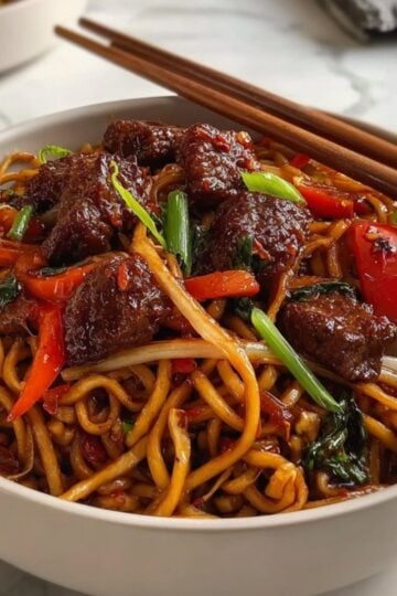A professional food photography shot of Beijing Beef Noodles topped with fresh green onions, served in a white bowl with wooden chopsticks.