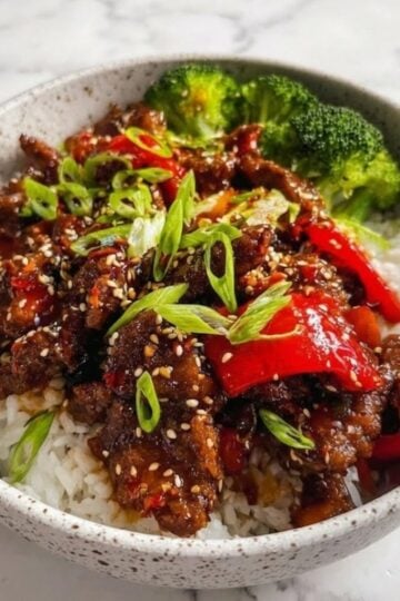 A full bowl of Beijing Beef stir fry served with steamed white rice and a side of bright green broccoli florets.