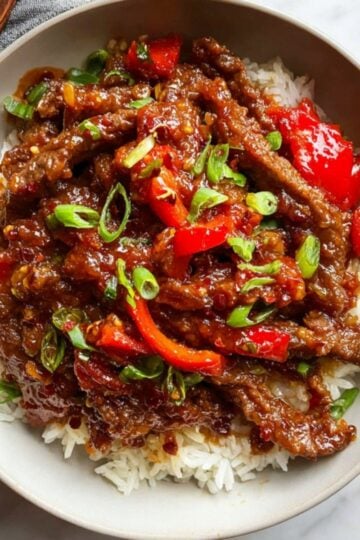 A top-down view of the completed Beijing Beef dish served in a bowl with rice and wooden chopsticks on the side.