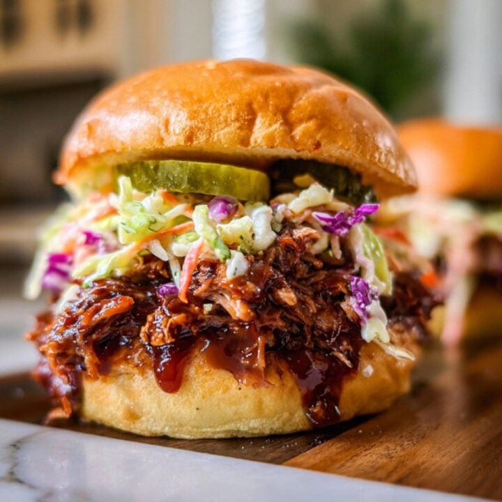 A towering brisket sandwich on a brioche bun, featuring layers of saucy meat, pickles, and colorful coleslaw.