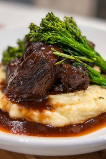 Close-up of a plated Wagyu Beef Cheeks Recipe featuring rich gravy, mashed potatoes, and steamed green vegetables.