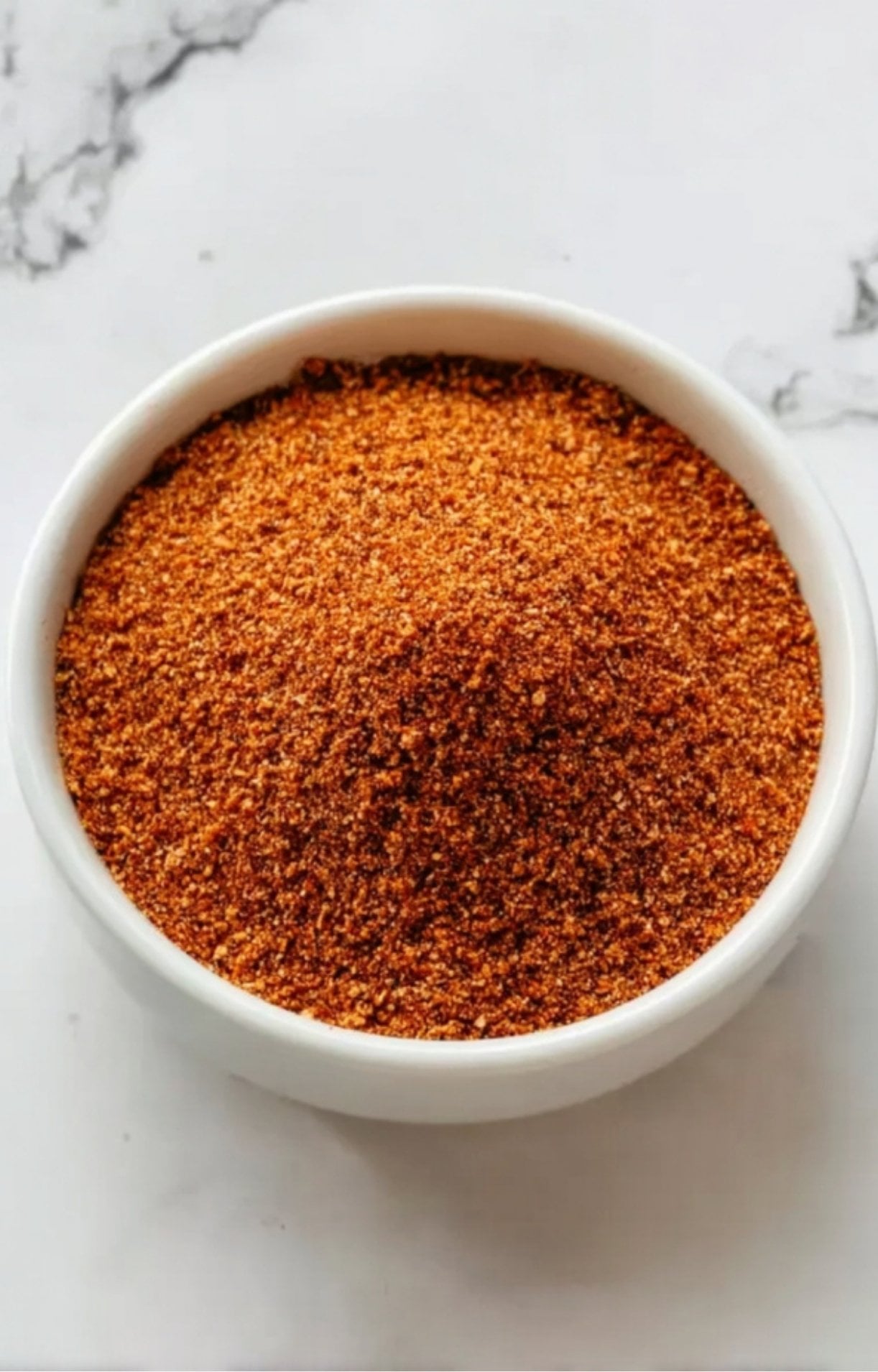 A top-down view of a small white ceramic bowl filled with a finely blended, reddish-brown smoked beef brisket rub.