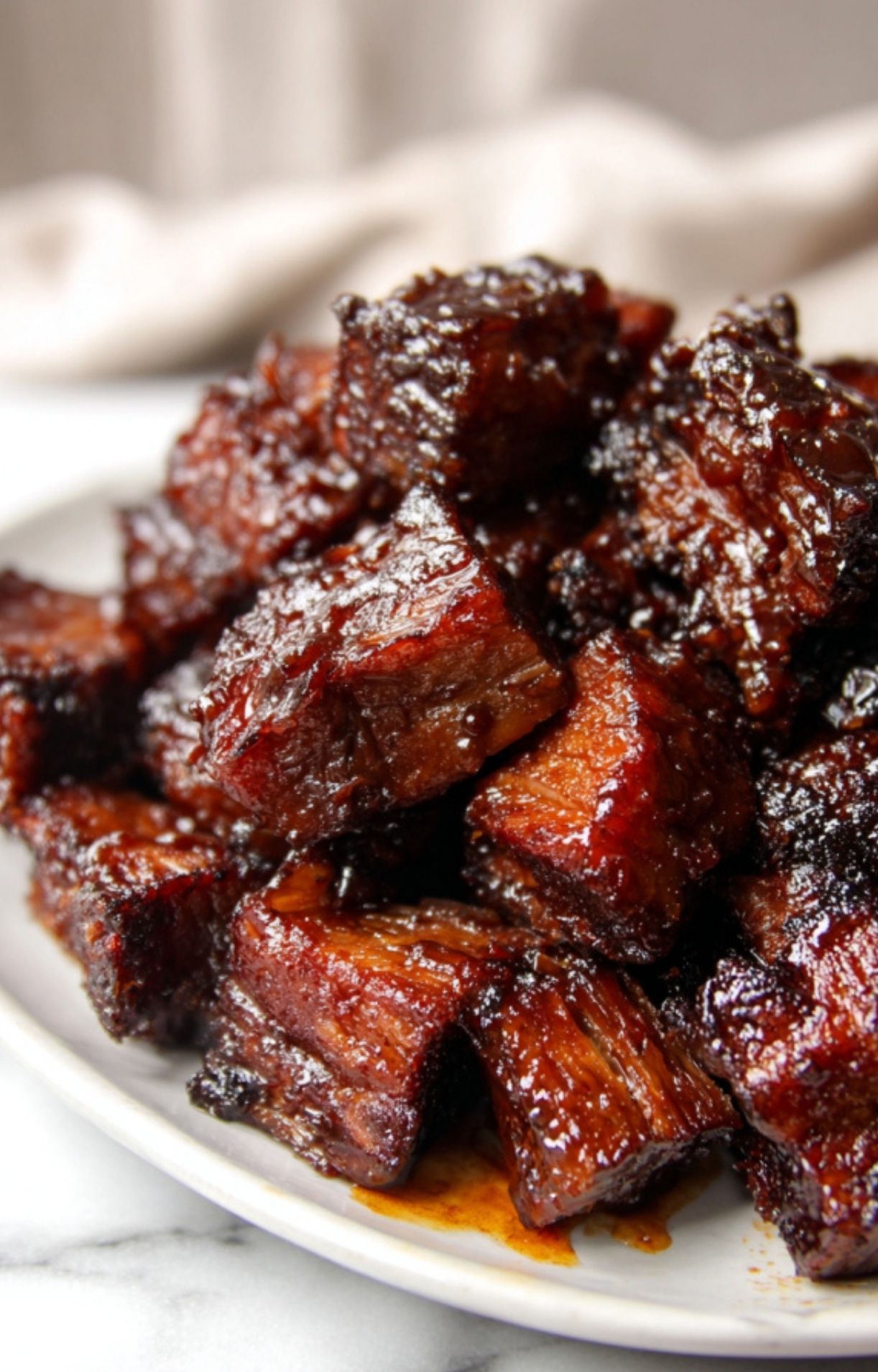 A close-up of juicy, tender Smoked Beef Brisket Burnt Ends stacked on a white plate with visible fat rendering.