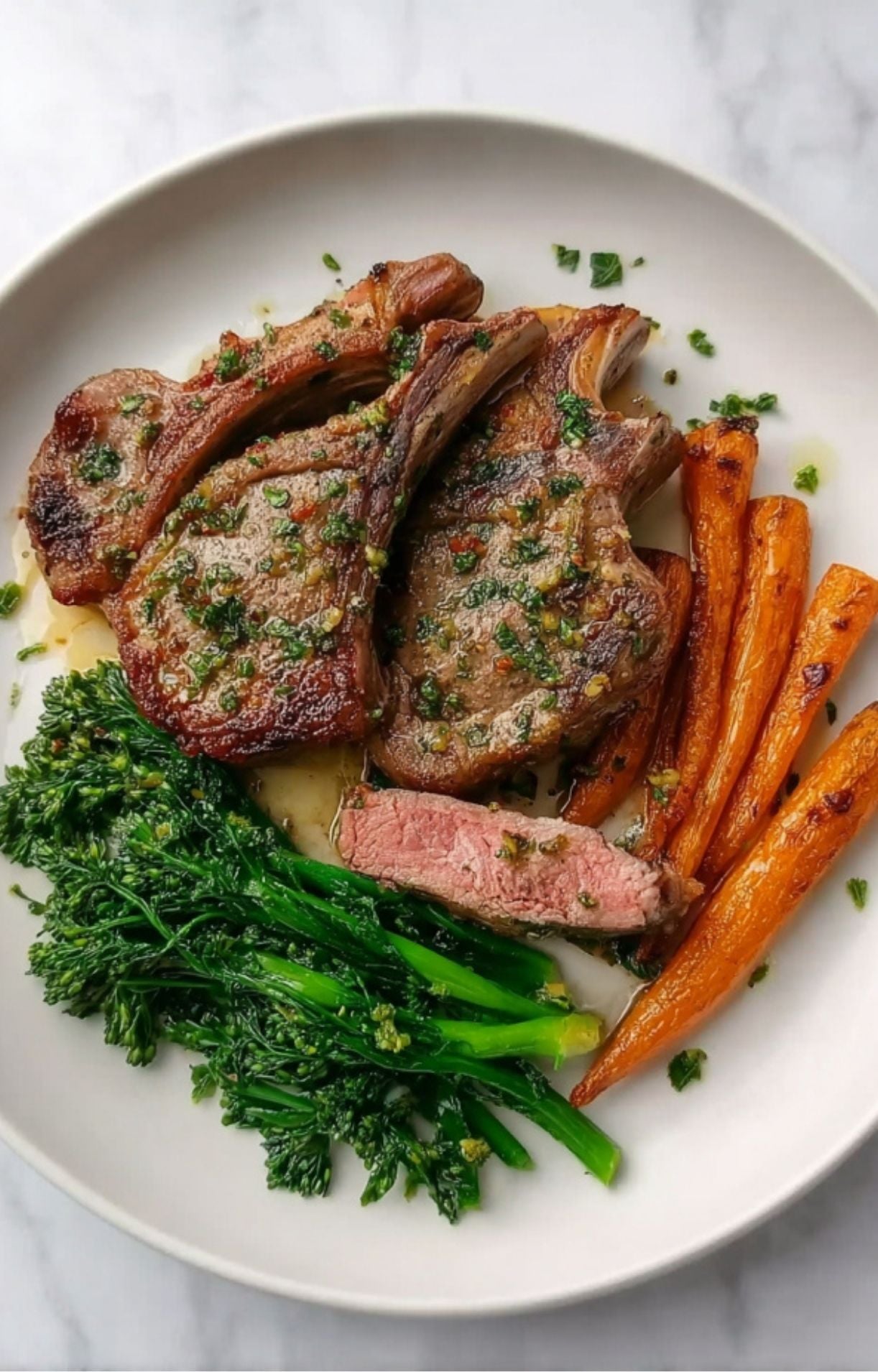 A complete meal featuring tender lamb chops with a medium-pink center, served alongside roasted honey-glazed carrots and steamed broccolini.