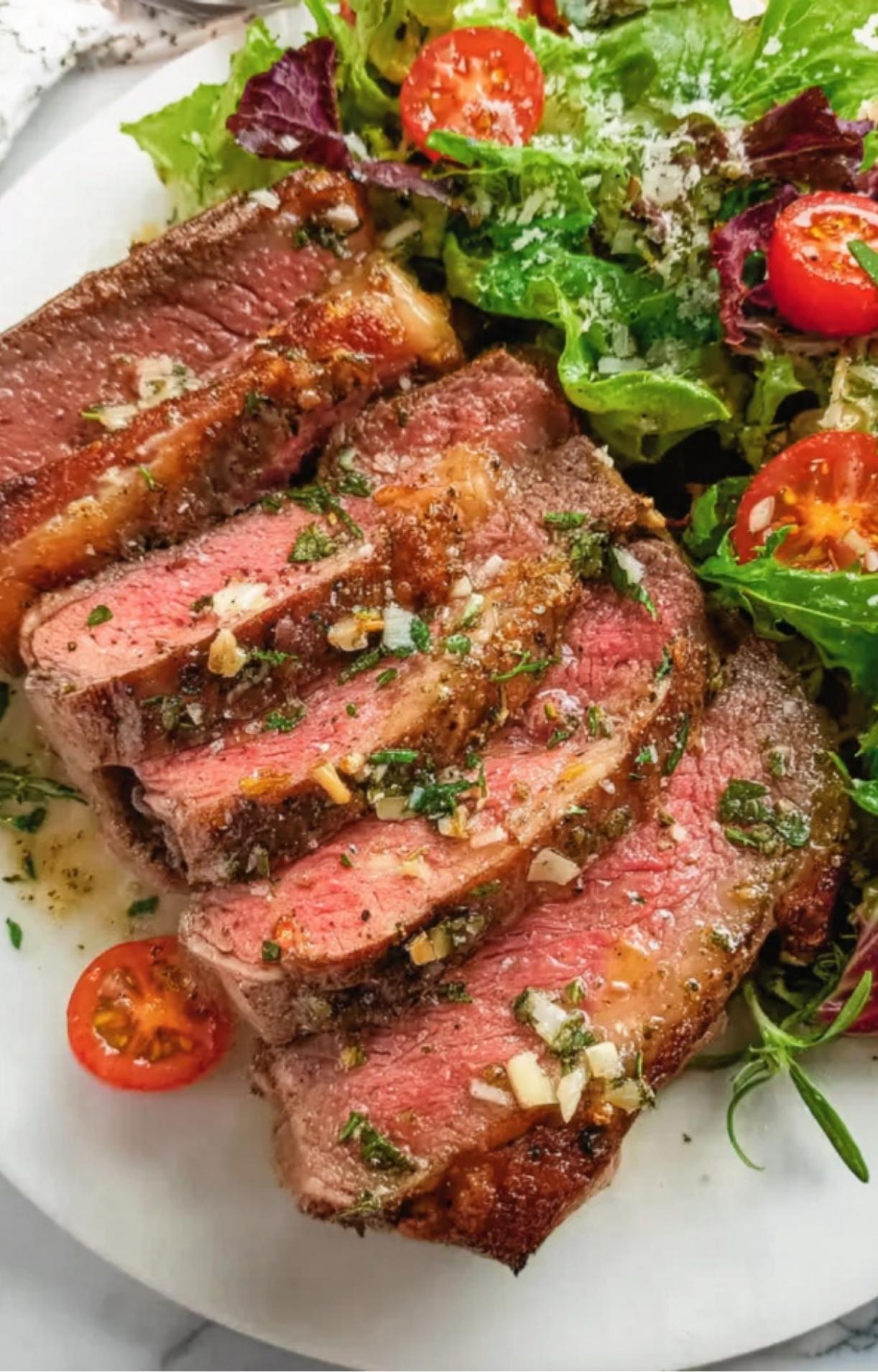 Sliced smoked tomahawk steak served with a fresh garden salad and cherry tomatoes.