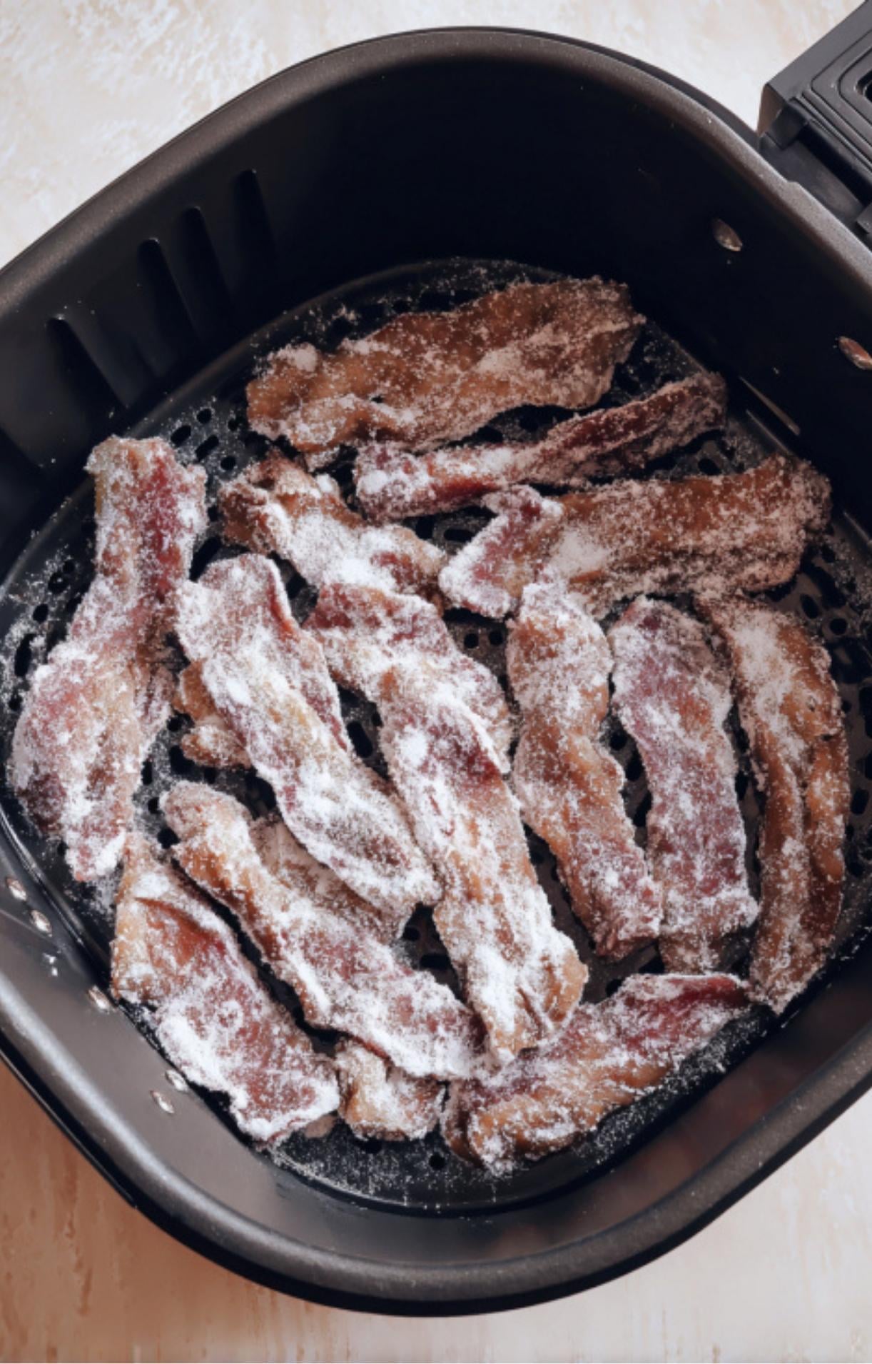 Floured beef strips arranged in a single layer inside a black air fryer basket ready for cooking.