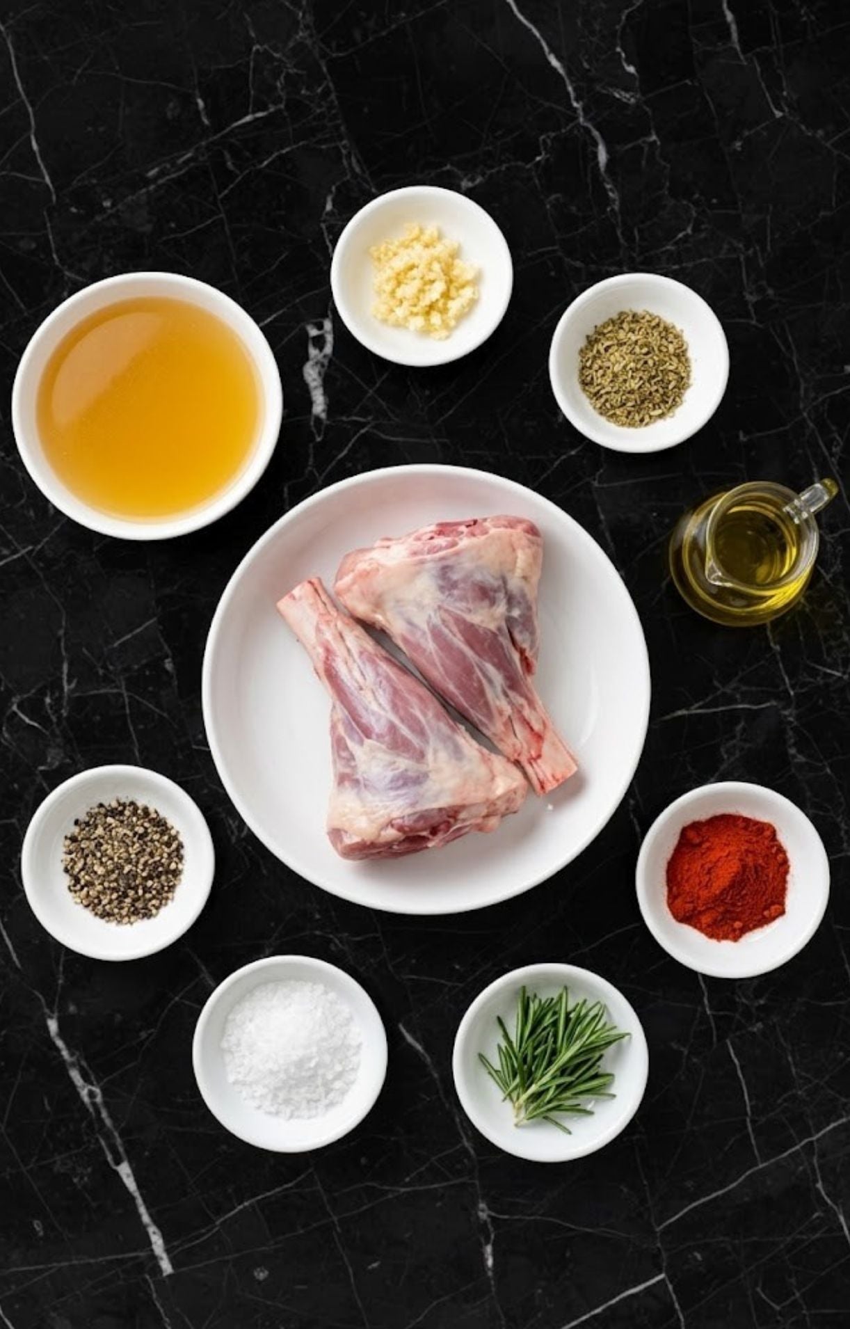 A top-down view of raw lamb shanks, olive oil, beef broth, garlic, rosemary, and spices on a black marble surface.