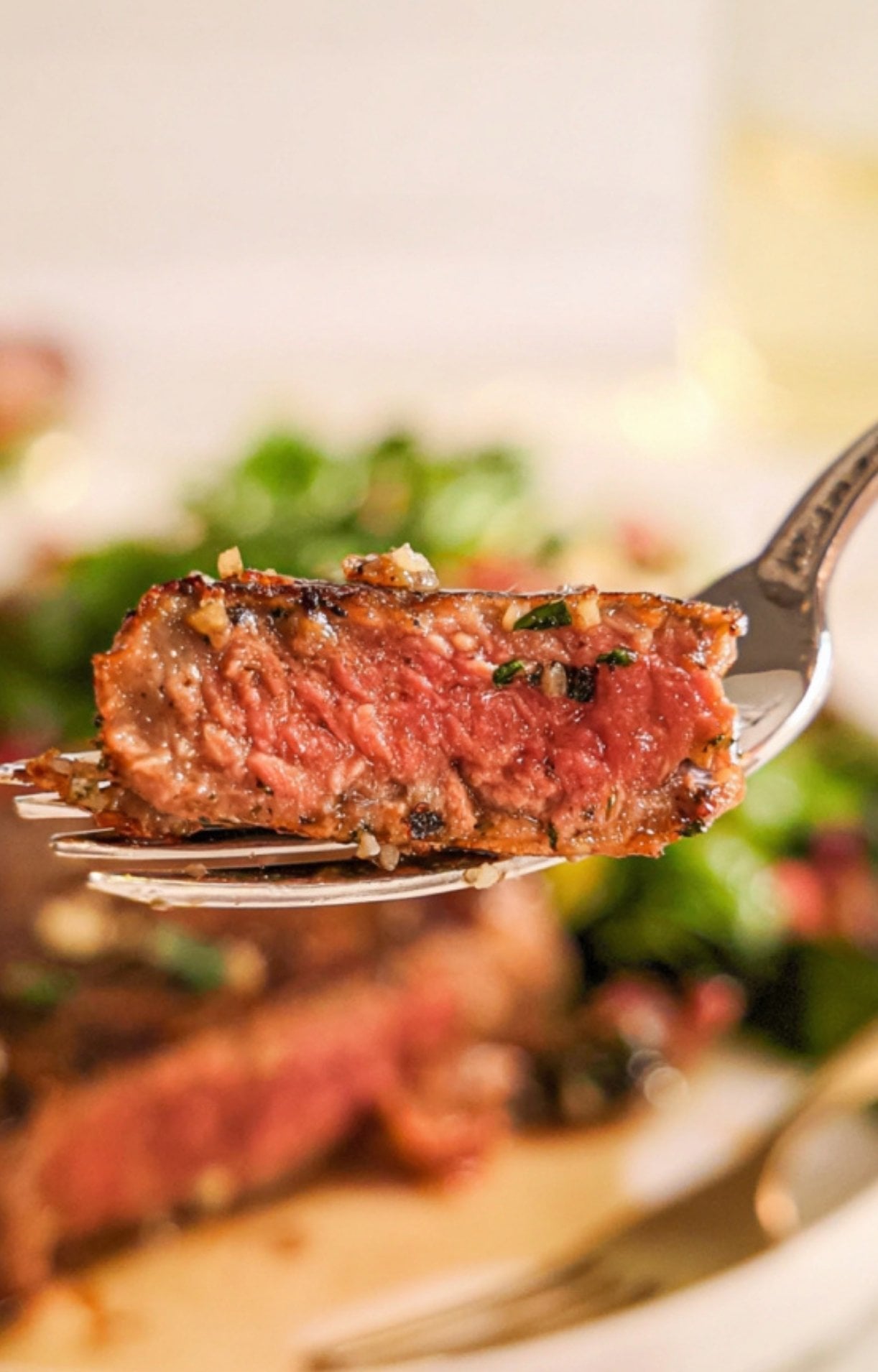 A single slice of juicy smoked tomahawk steak held up on a fork with garlic and herbs.