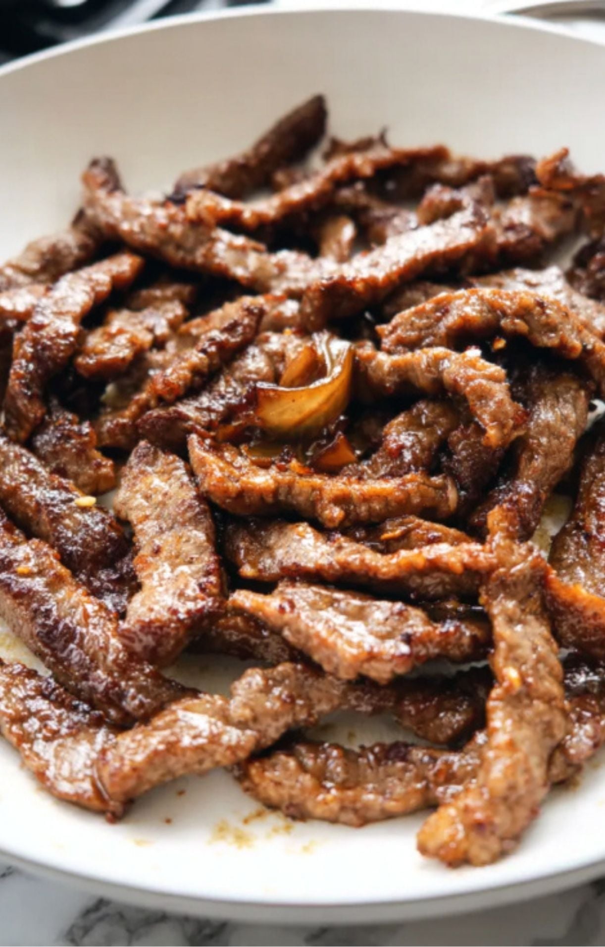 Thinly sliced beef strips browned and crisped in a skillet, showing a caramelized exterior.