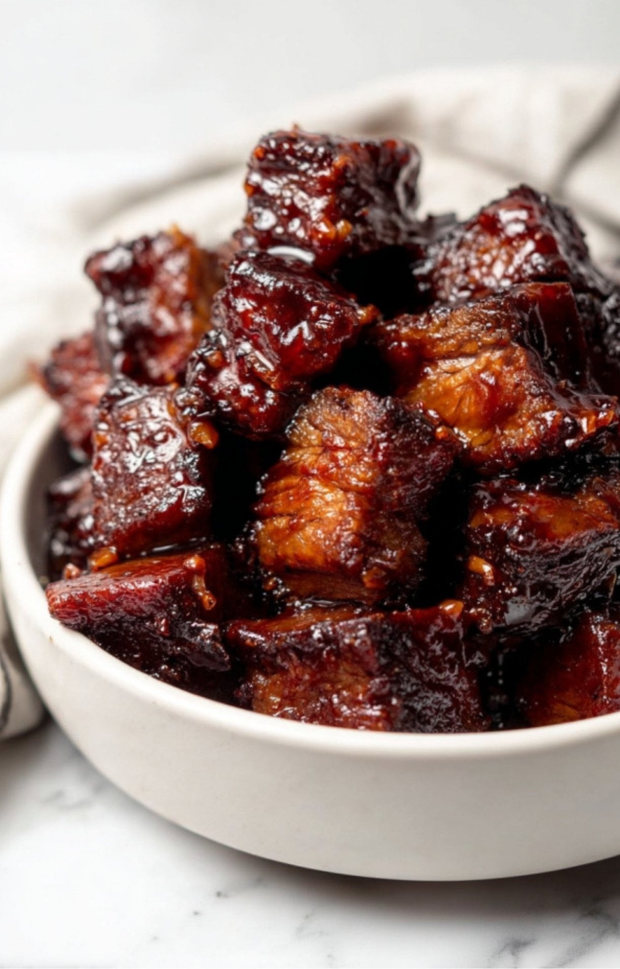 A white bowl filled with bite-sized, tender Smoked Beef Brisket Burnt Ends with a deep mahogany color.