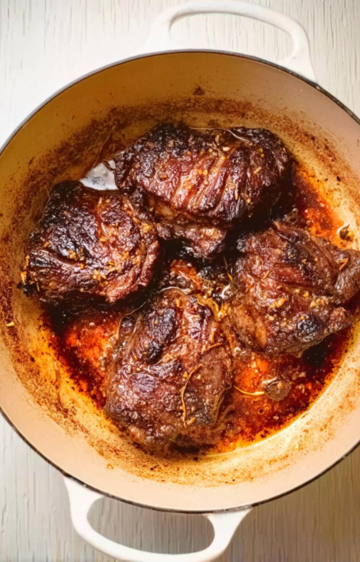 Beef cheeks being seared until deep golden brown in a white Dutch oven to lock in flavor.