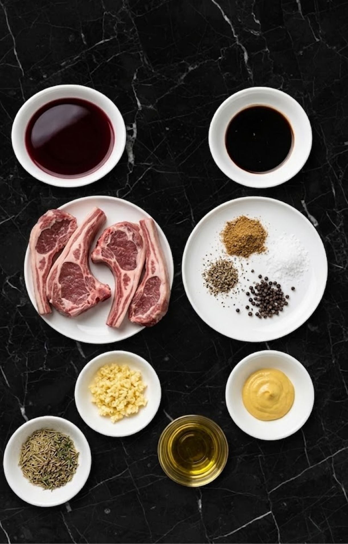 A flat lay of ingredients including raw lamb, rosemary, garlic, mustard, oil, and spices in small white bowls.